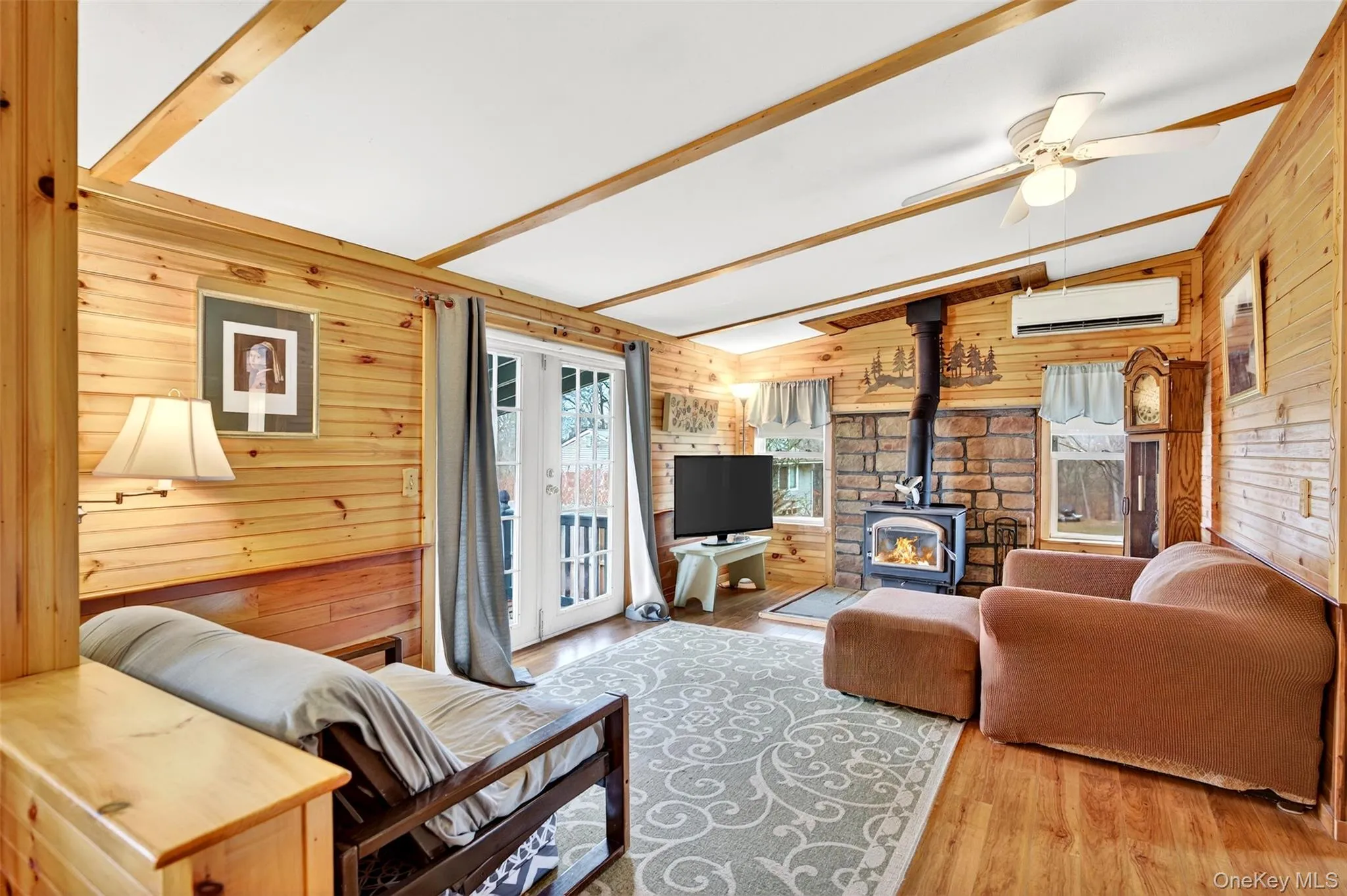 Living room featuring a wood stove, wooden walls, ceiling fan, wood finished floors, and vaulted ceiling Living room featuring a wood stove, wooden walls, ceiling fan, wood finished floors, and vaulted ceiling