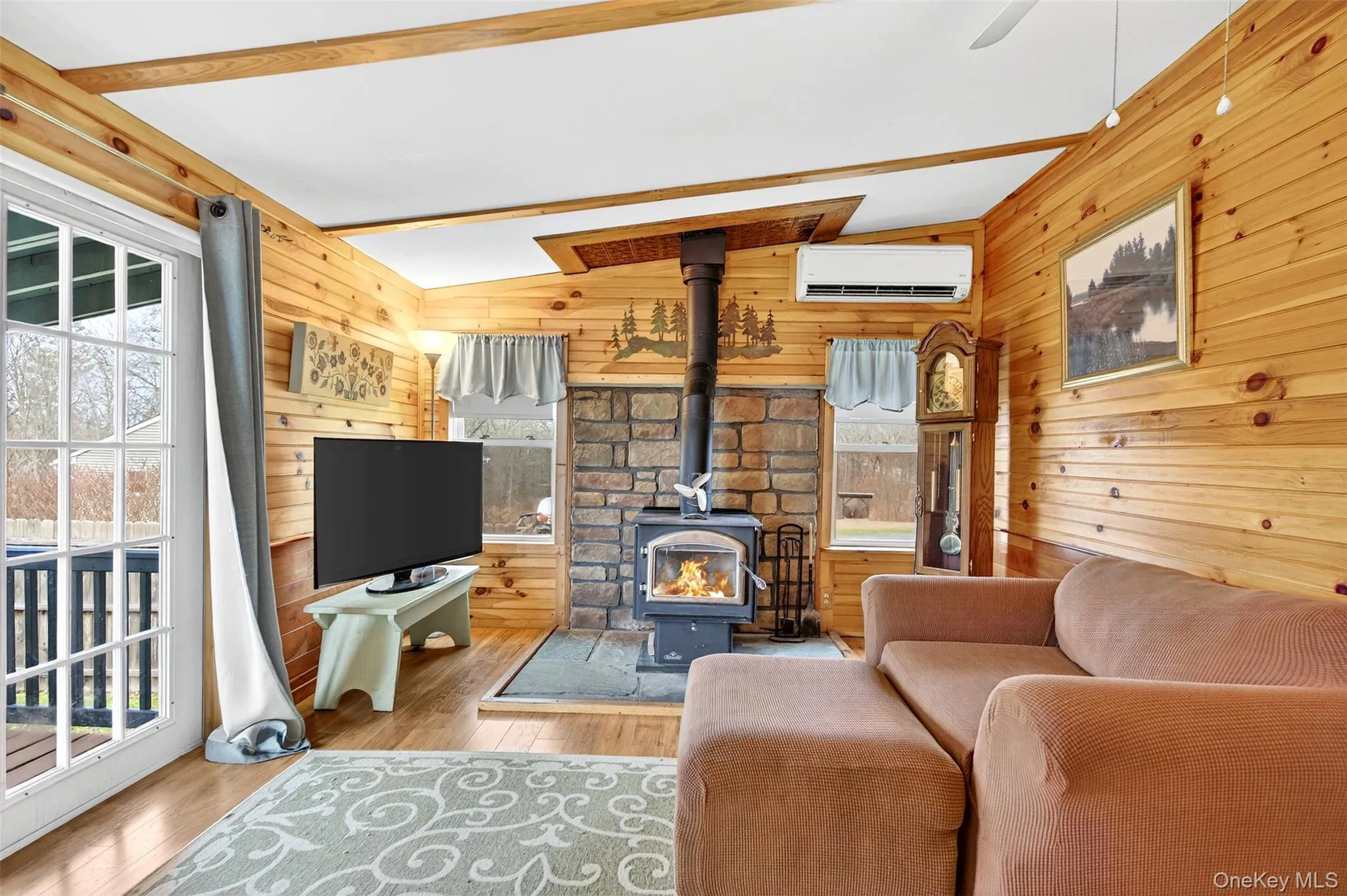 Living room featuring a wood stove, vaulted ceiling, hardwood / wood-style flooring, a wall unit AC, and a ceiling fan Living room featuring a wood stove, vaulted ceiling, hardwood / wood-style flooring, a wall unit AC, and a ceiling fan
