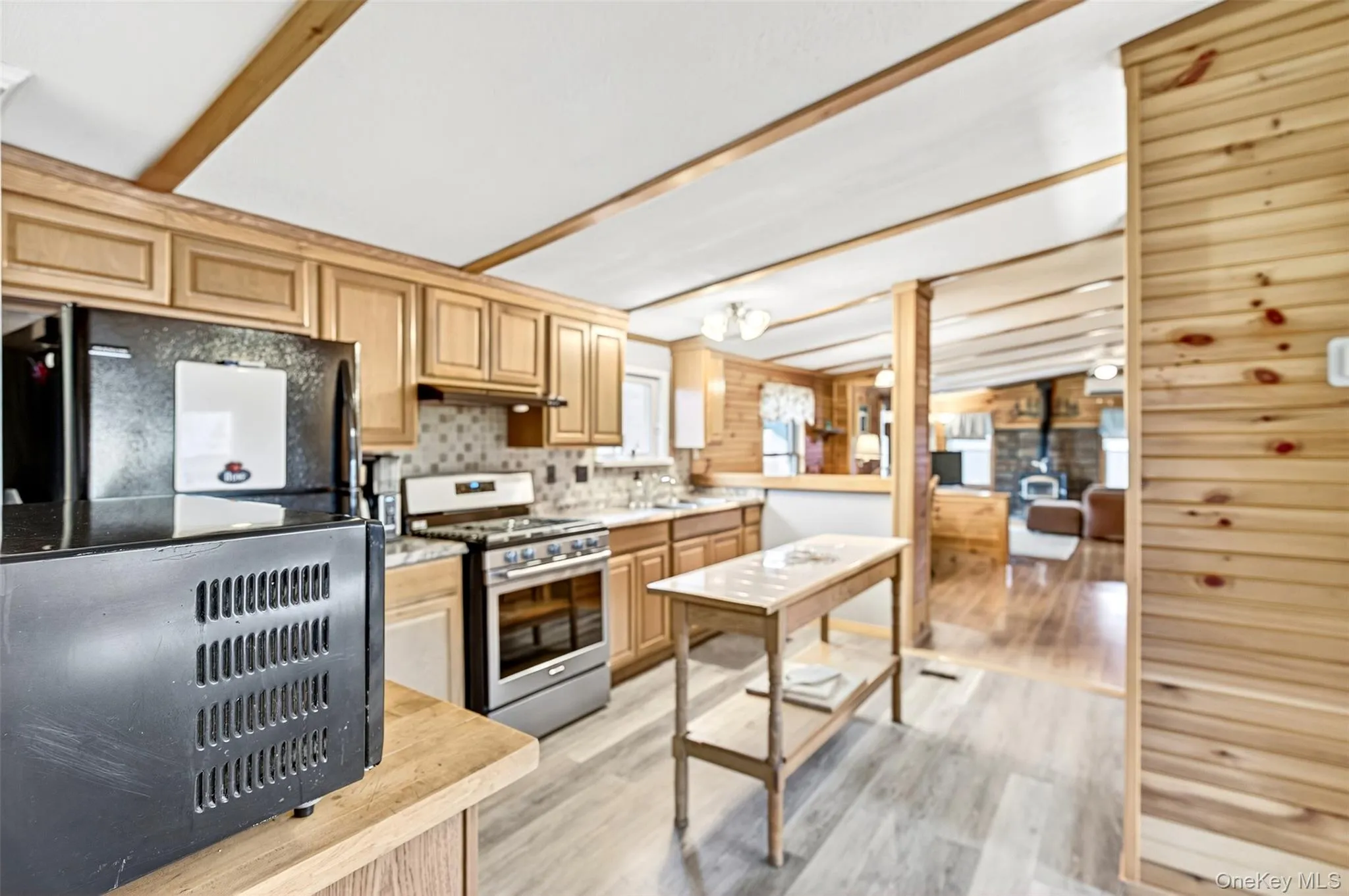 Kitchen featuring black fridge, light wood finished floors, stainless steel gas range oven, light brown cabinets, and wood walls Kitchen featuring black fridge, light wood finished floors, stainless steel gas range oven, light brown cabinets, and wood walls