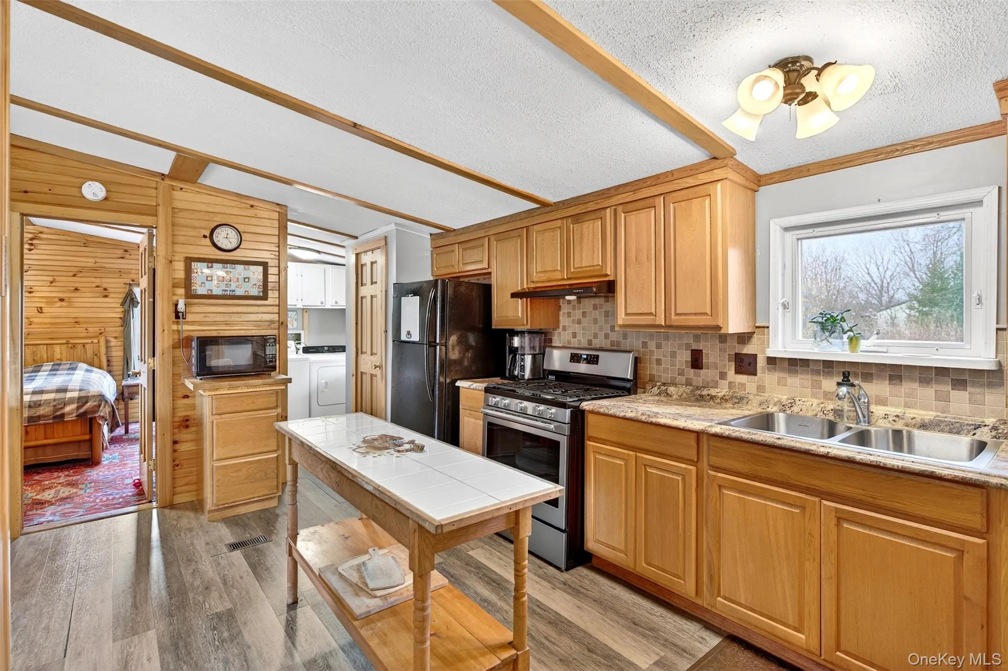 Kitchen featuring black appliances, light countertops, light wood-style flooring, backsplash, and lofted ceiling Kitchen featuring black appliances, light countertops, light wood-style flooring, backsplash, and lofted ceiling