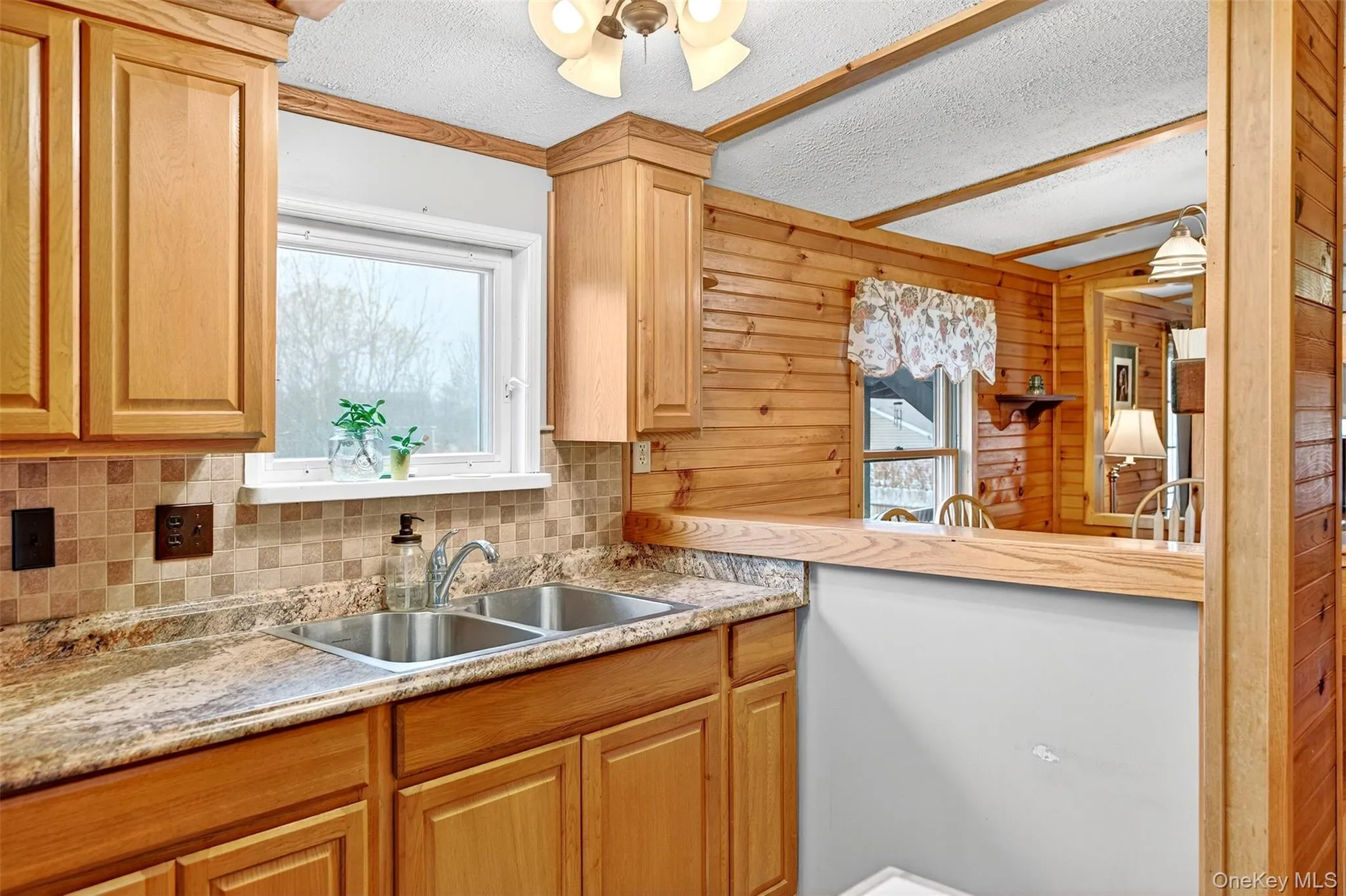 Kitchen with a textured ceiling, tasteful backsplash, plenty of natural light, and brown cabinets Kitchen with a textured ceiling, tasteful backsplash, plenty of natural light, and brown cabinets