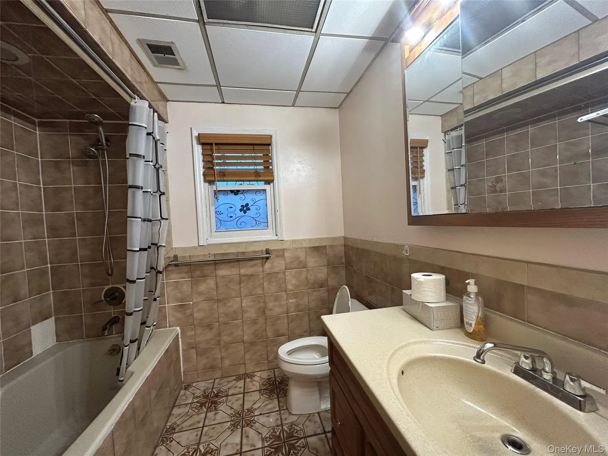 Full bathroom featuring vanity, tiled shower / bath combo, light tile patterned floors, tile walls, and a drop ceiling Full bathroom featuring vanity, tiled shower / bath combo, light tile patterned floors, tile walls, and a drop ceiling