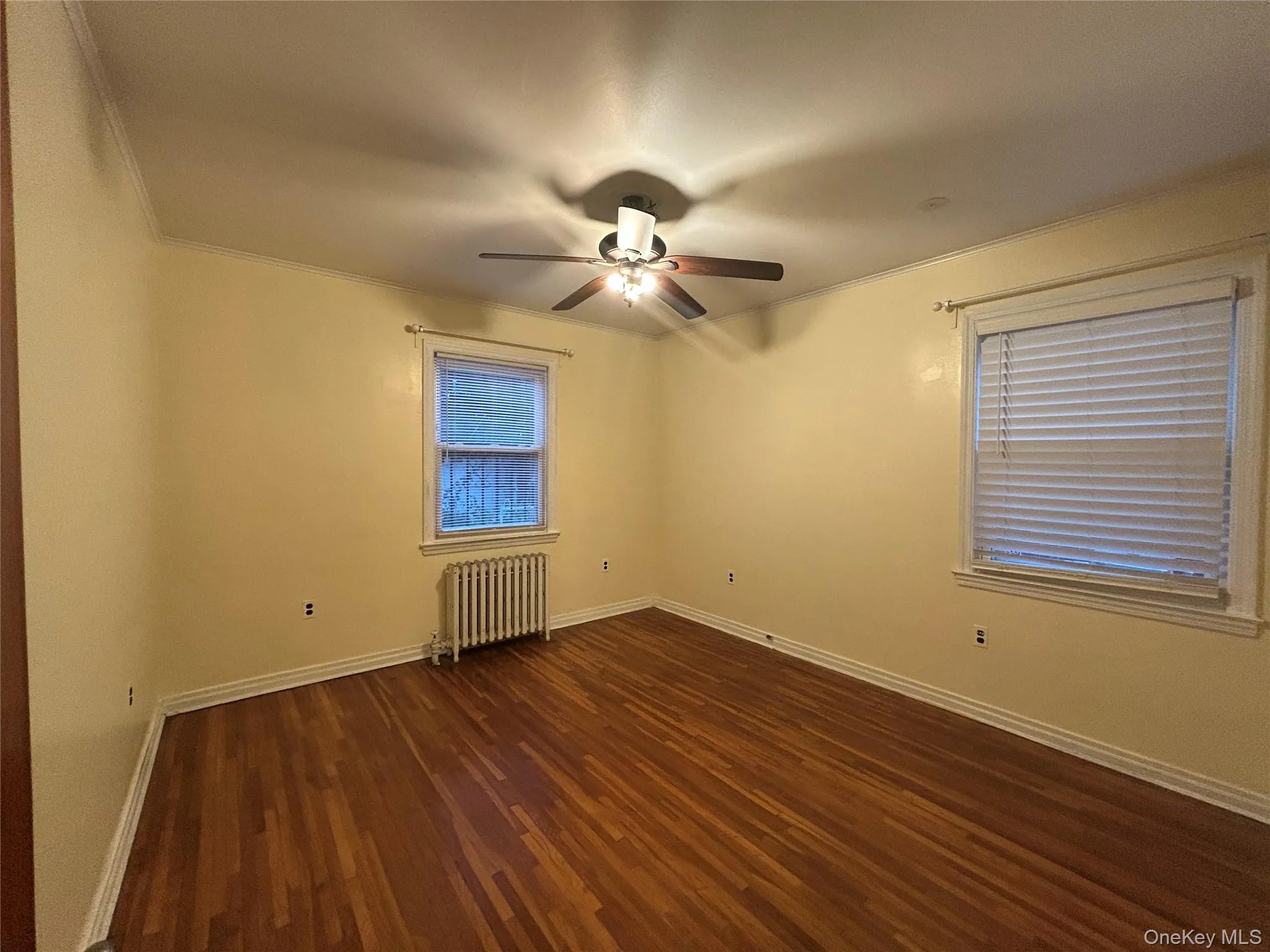 Spare room featuring dark wood finished floors, radiator heating unit, crown molding, and a ceiling fan Spare room featuring dark wood finished floors, radiator heating unit, crown molding, and a ceiling fan