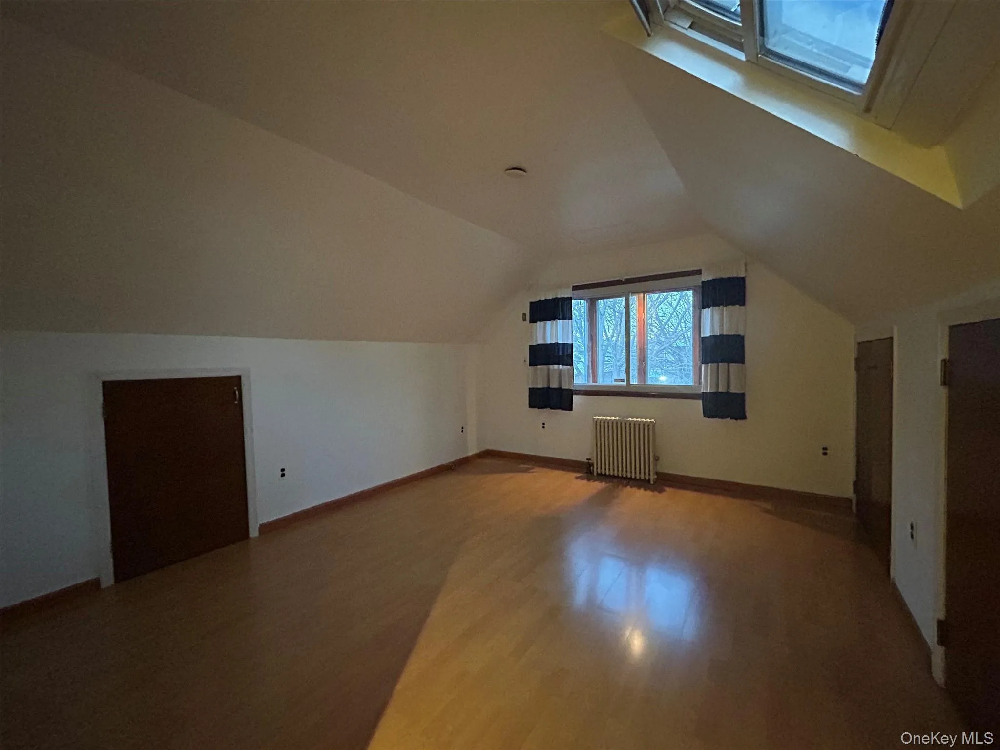 Bonus room featuring radiator, wood finished floors, vaulted ceiling, and a skylight Bonus room featuring radiator, wood finished floors, vaulted ceiling, and a skylight