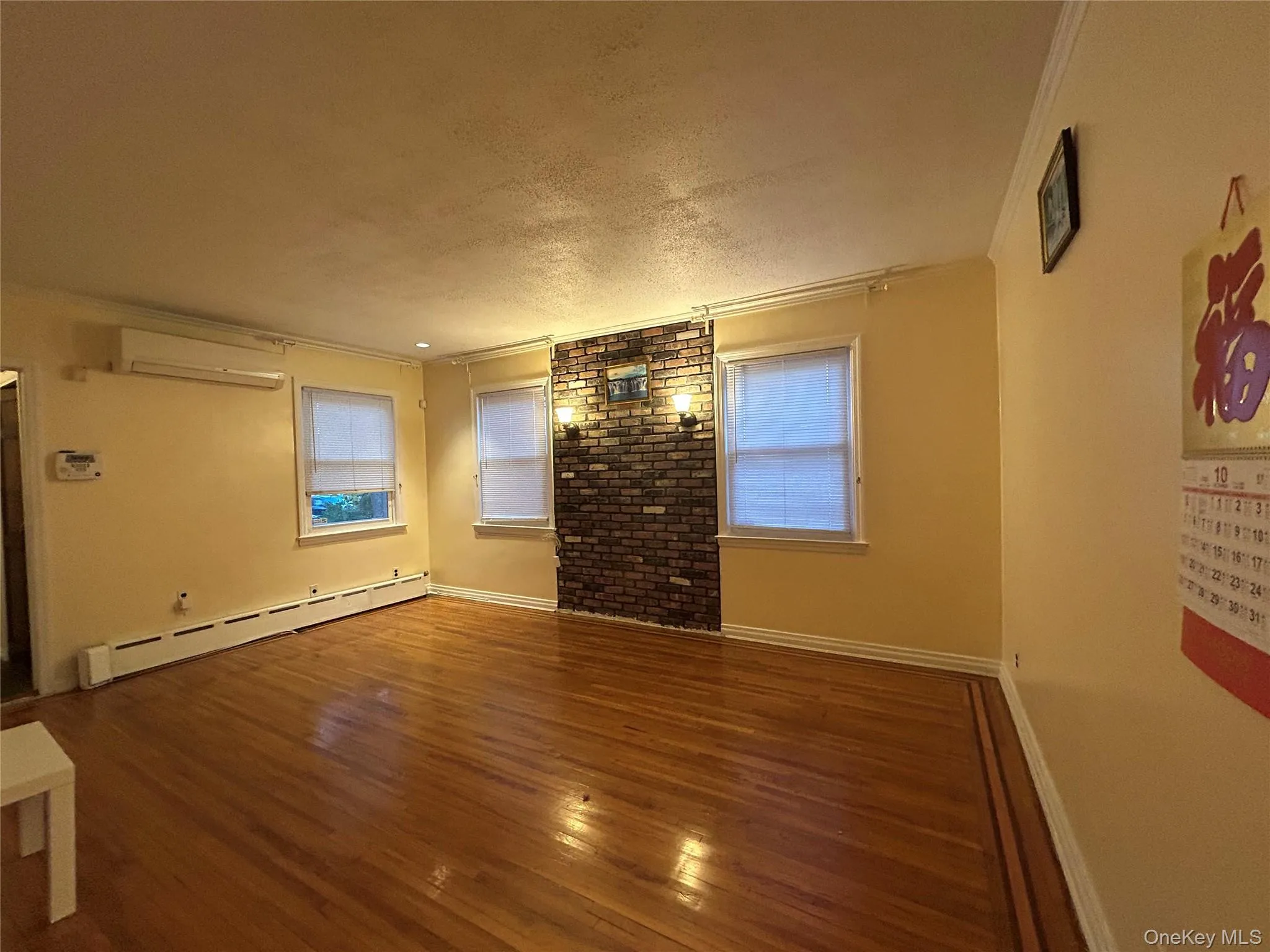 Spare room with crown molding, a textured ceiling, baseboard heating, hardwood / wood-style floors, and a wall unit AC Spare room with crown molding, a textured ceiling, baseboard heating, hardwood / wood-style floors, and a wall unit AC