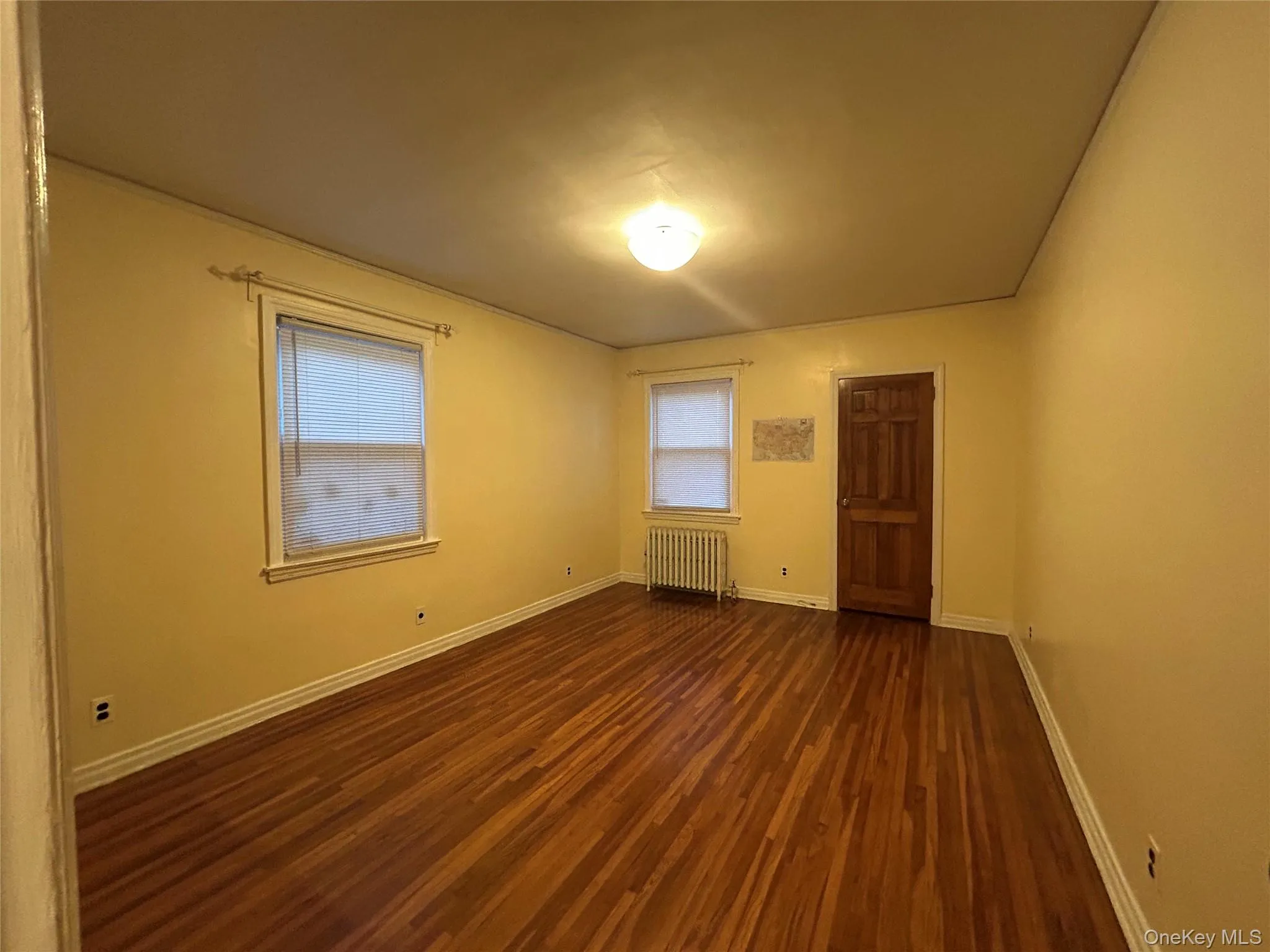 Spare room featuring dark wood-style floors and radiator heating unit Spare room featuring dark wood-style floors and radiator heating unit