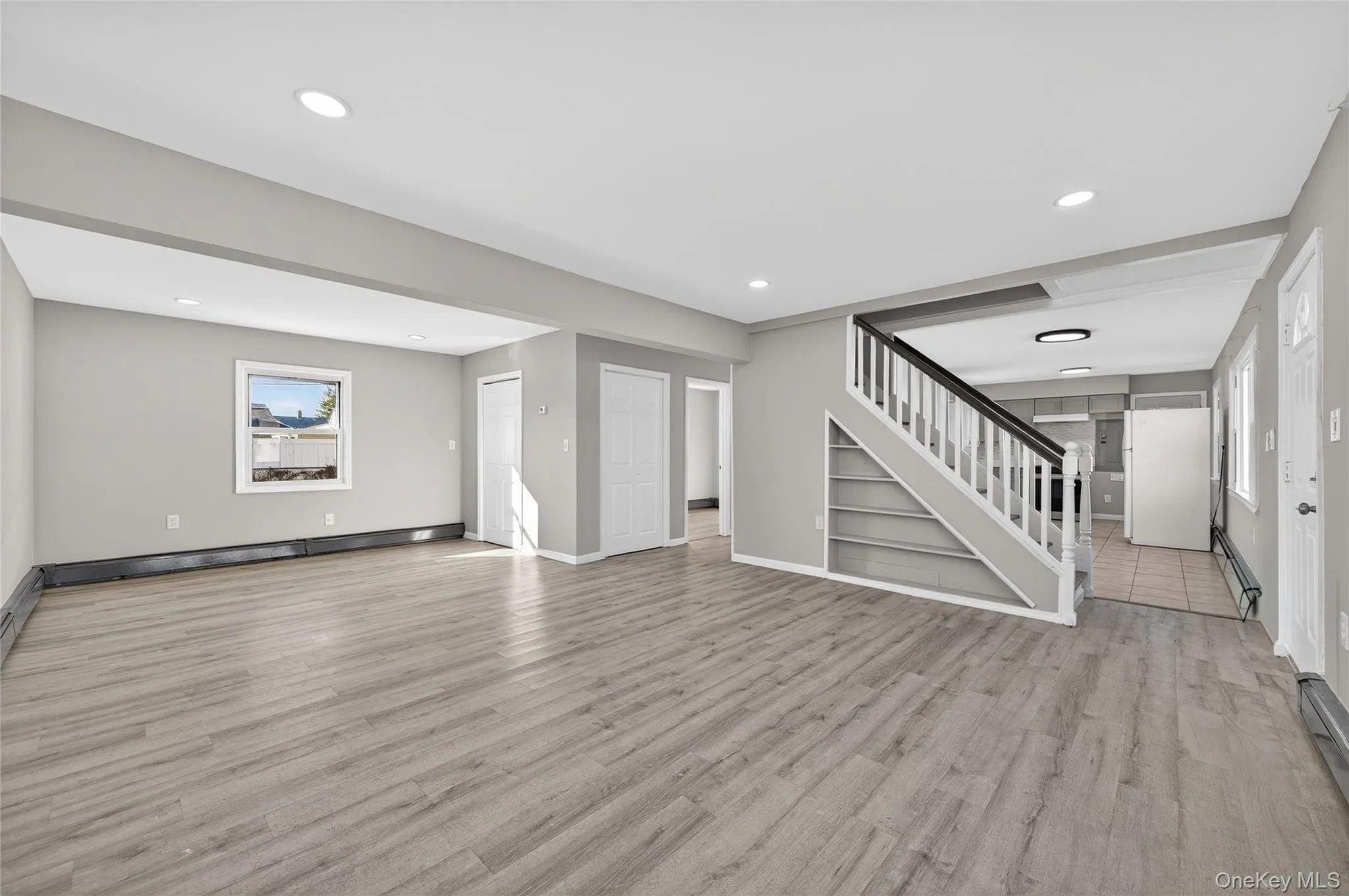 Unfurnished living room with light wood-type flooring, stairway, a baseboard heating unit, and recessed lighting Unfurnished living room with light wood-type flooring, stairway, a baseboard heating unit, and recessed lighting
