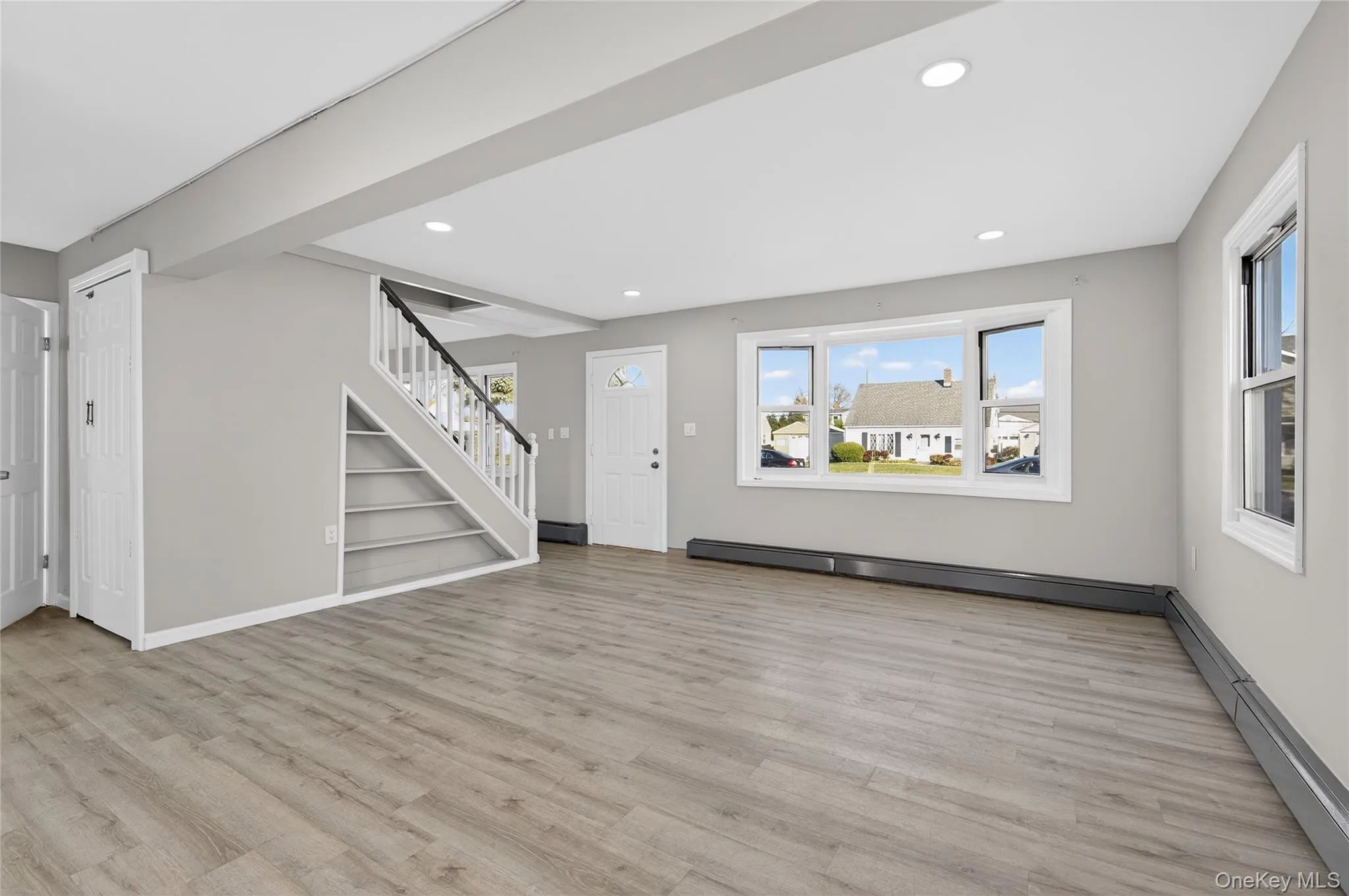 Unfurnished living room with stairway, baseboard heating, light wood finished floors, recessed lighting, and built in shelves Unfurnished living room with stairway, baseboard heating, light wood finished floors, recessed lighting, and built in shelves