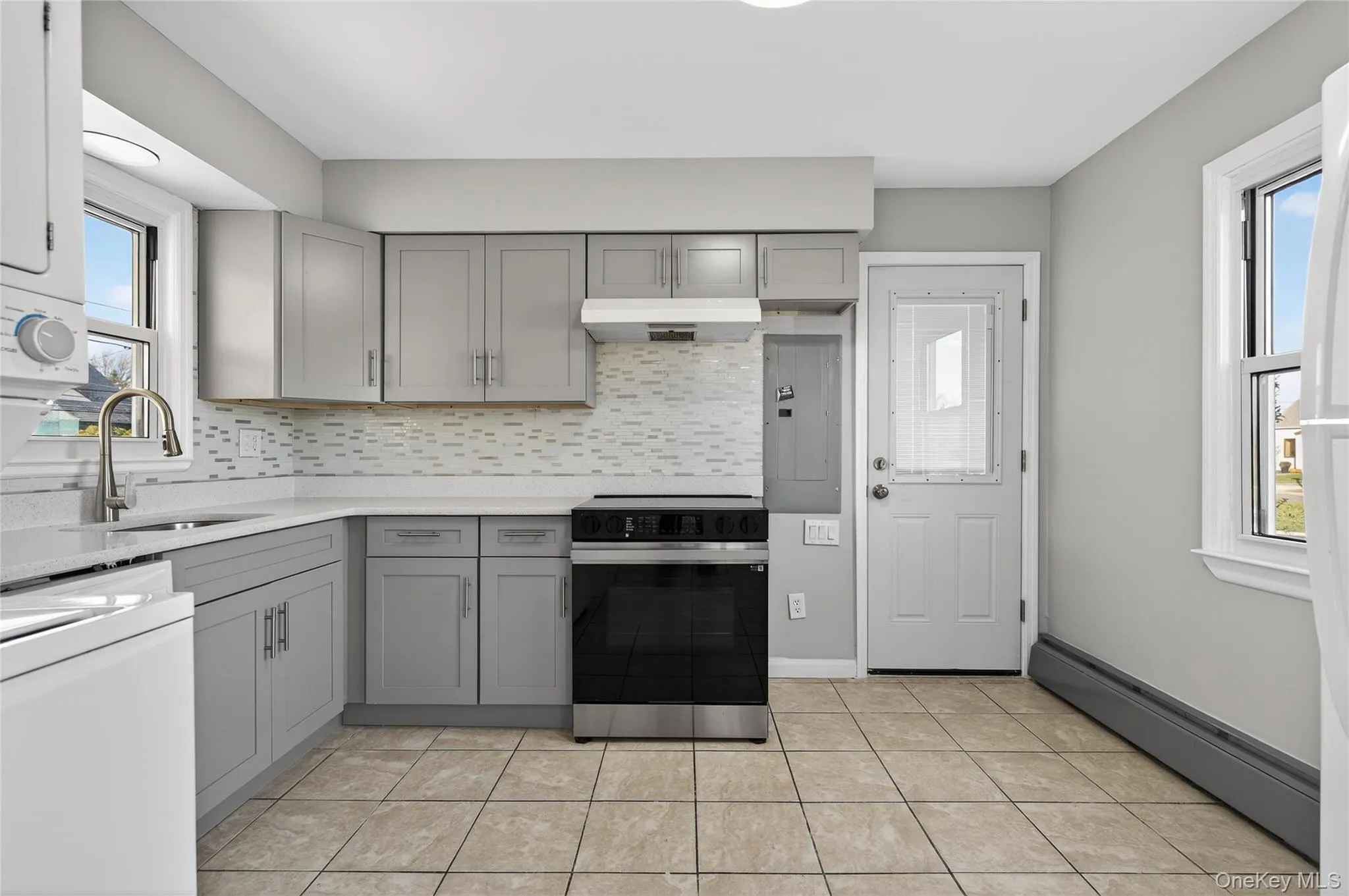 Kitchen with gray cabinets, electric stove, baseboard heating, electric panel, and under cabinet range hood Kitchen with gray cabinets, electric stove, baseboard heating, electric panel, and under cabinet range hood