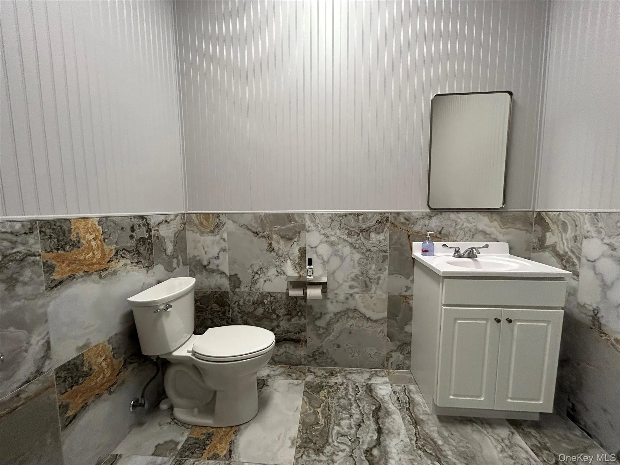 Bathroom with tile walls, vanity, light marble finish flooring, and wainscoting Bathroom with tile walls, vanity, light marble finish flooring, and wainscoting