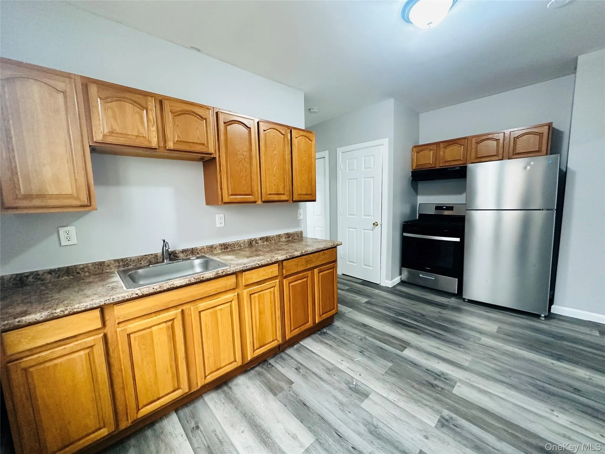 Kitchen featuring stainless steel appliances, under cabinet range hood, brown cabinetry, and light wood-type flooring Kitchen featuring stainless steel appliances, under cabinet range hood, brown cabinetry, and light wood-type flooring
