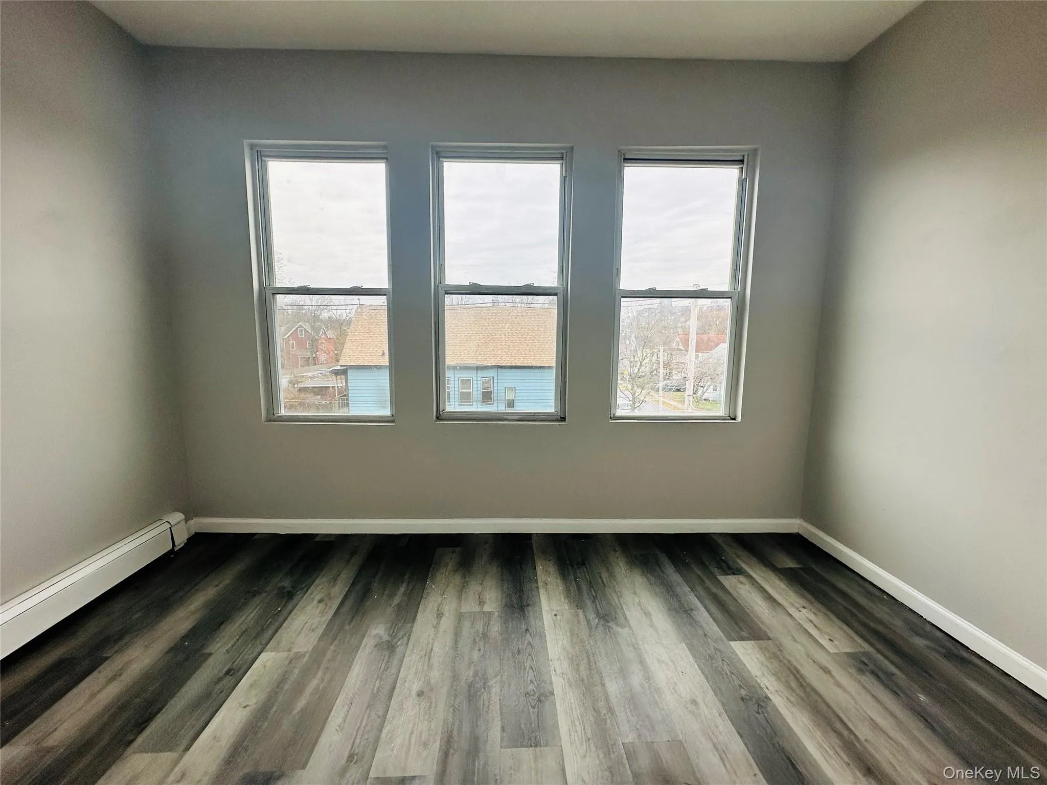 Empty room with dark wood-style flooring, plenty of natural light, and a baseboard heating unit Empty room with dark wood-style flooring, plenty of natural light, and a baseboard heating unit