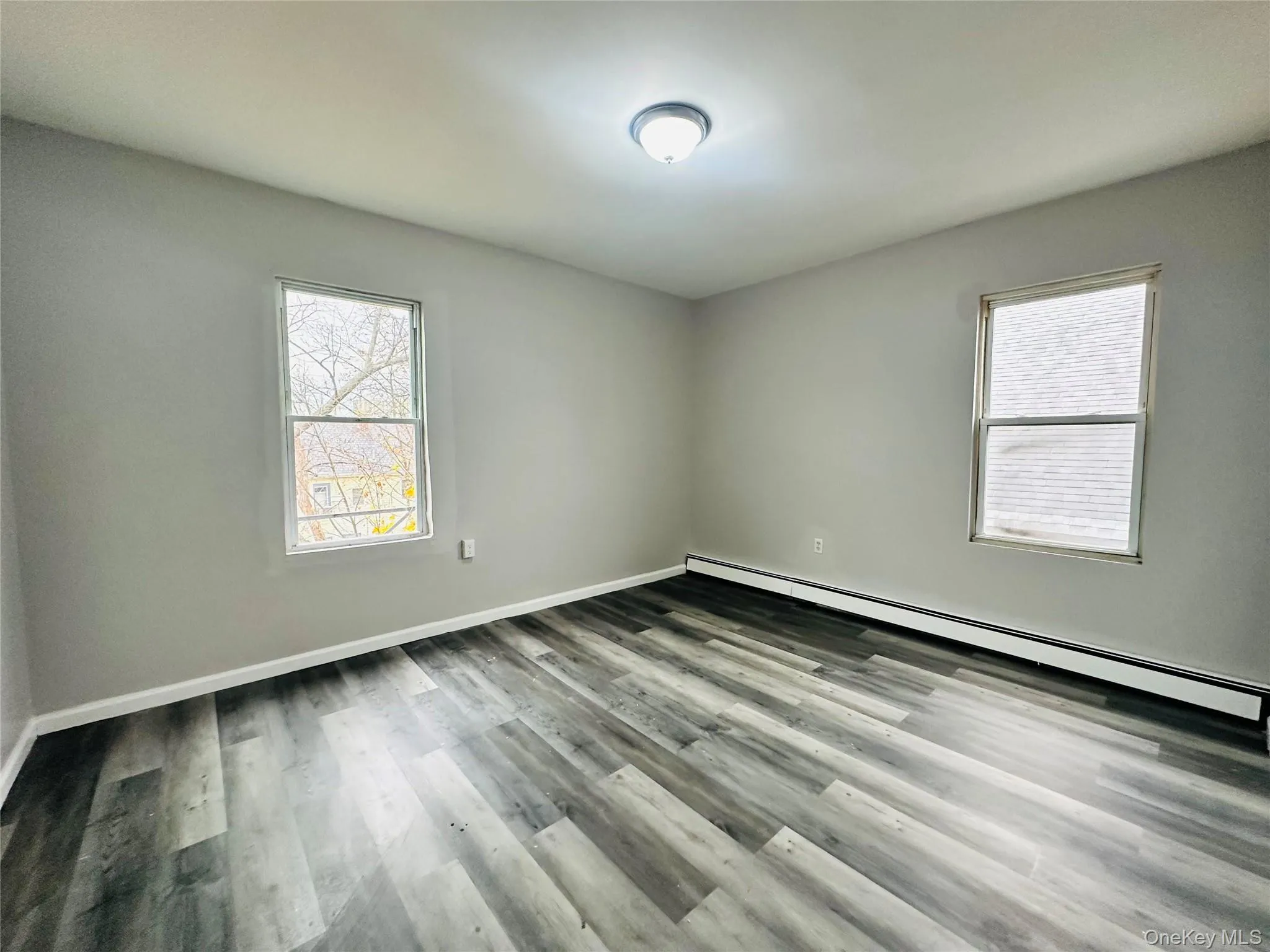 Empty room featuring baseboard heating, wood finished floors, and plenty of natural light Empty room featuring baseboard heating, wood finished floors, and plenty of natural light
