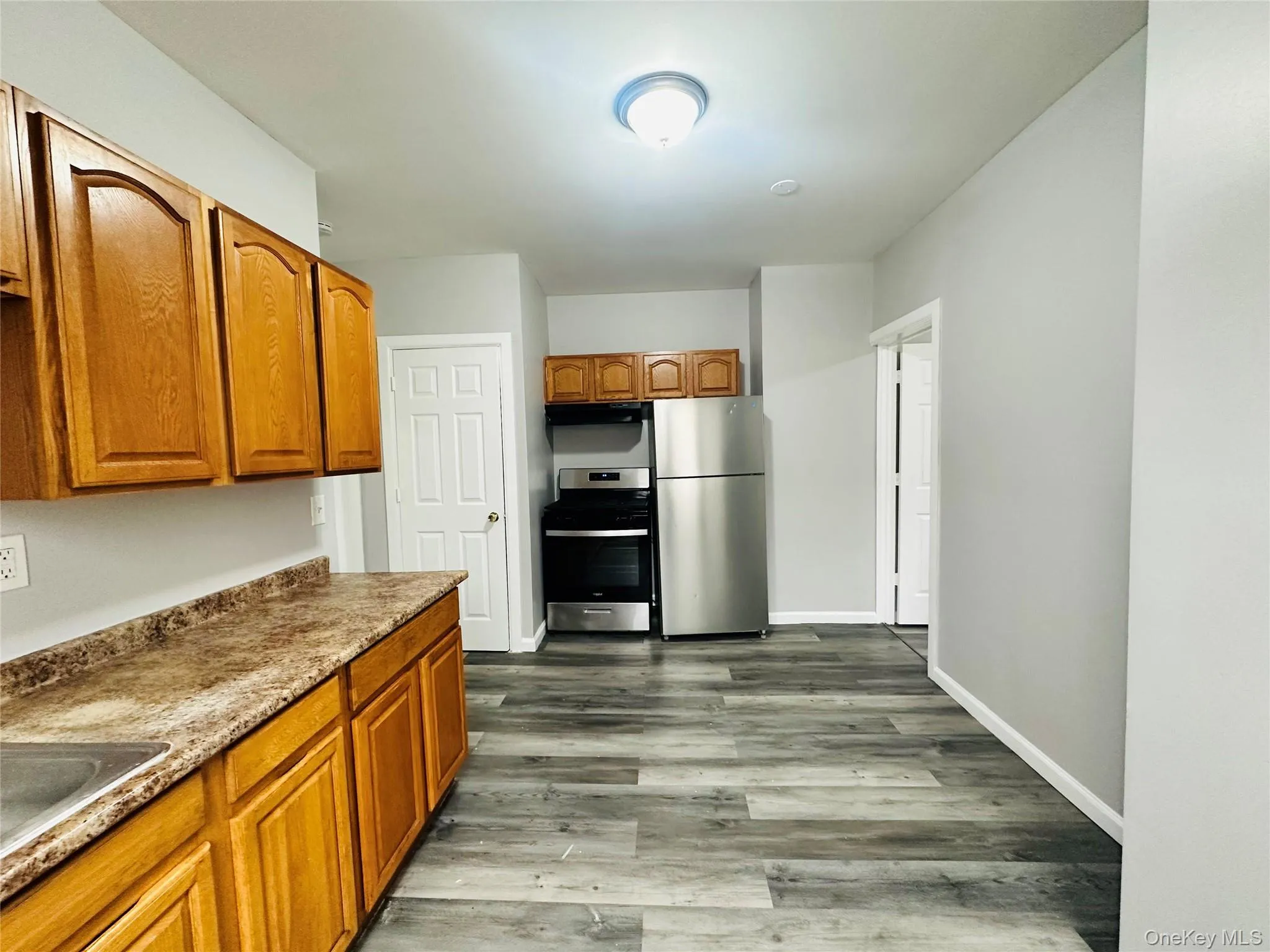 Kitchen with brown cabinets, stainless steel appliances, light wood-type flooring, under cabinet range hood, and light countertops Kitchen with brown cabinets, stainless steel appliances, light wood-type flooring, under cabinet range hood, and light countertops