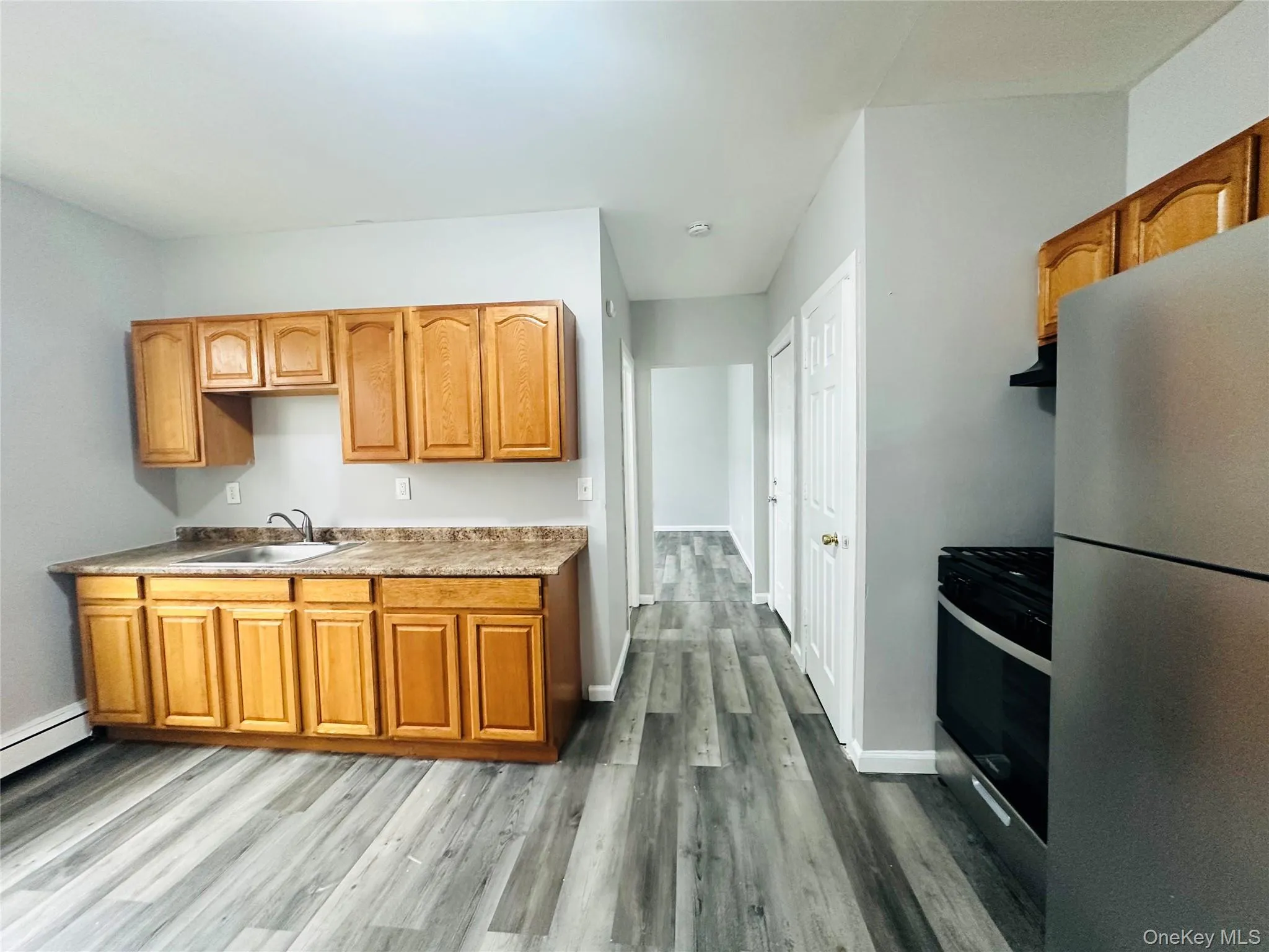 Kitchen featuring appliances with stainless steel finishes, light countertops, dark wood-style floors, brown cabinetry, and ventilation hood Kitchen featuring appliances with stainless steel finishes, light countertops, dark wood-style floors, brown cabinetry, and ventilation hood