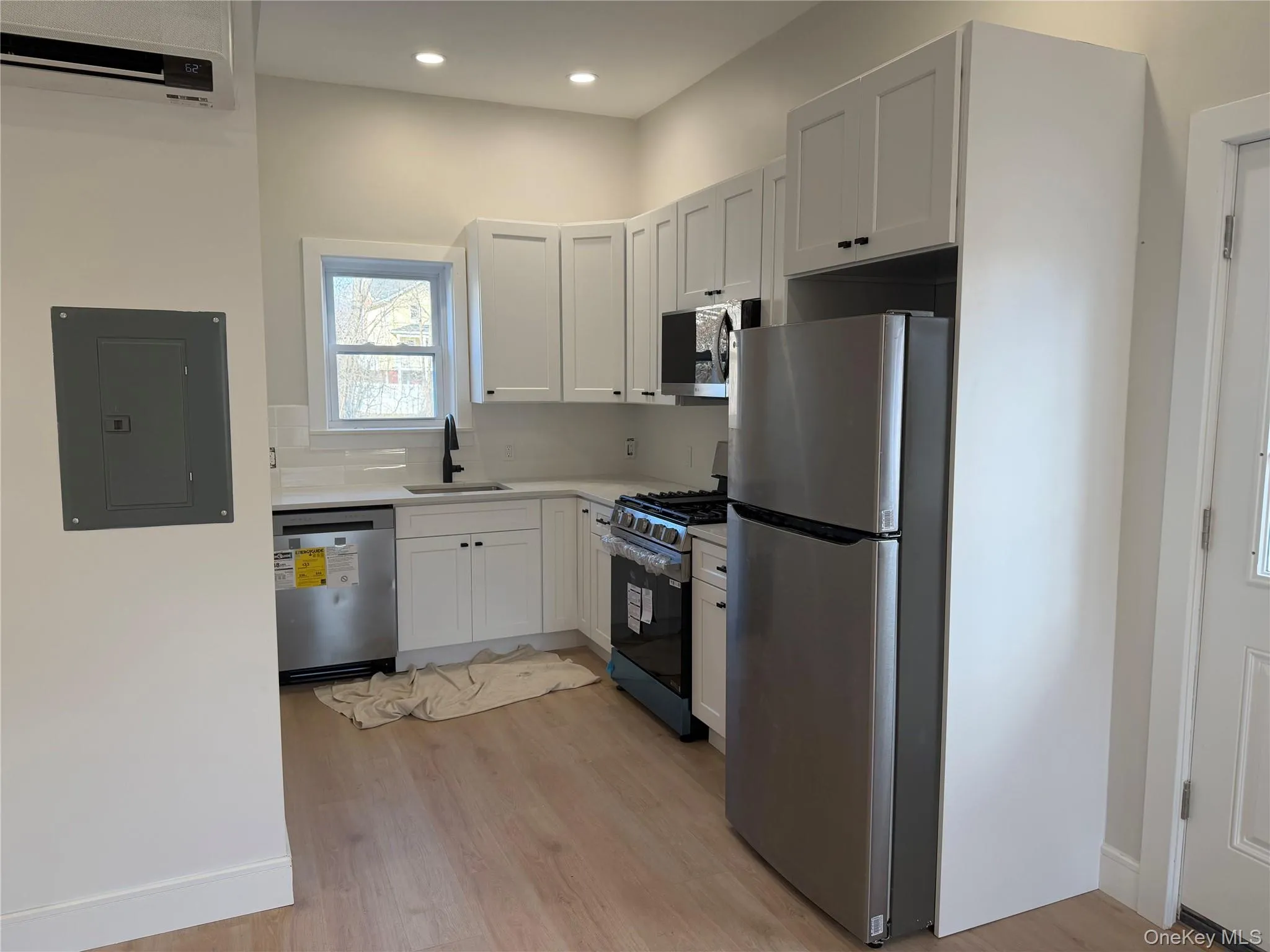 Kitchen with stainless steel appliances, white cabinetry, electric panel, a wall mounted AC, and light wood-type flooring Kitchen with stainless steel appliances, white cabinetry, electric panel, a wall mounted AC, and light wood-type flooring