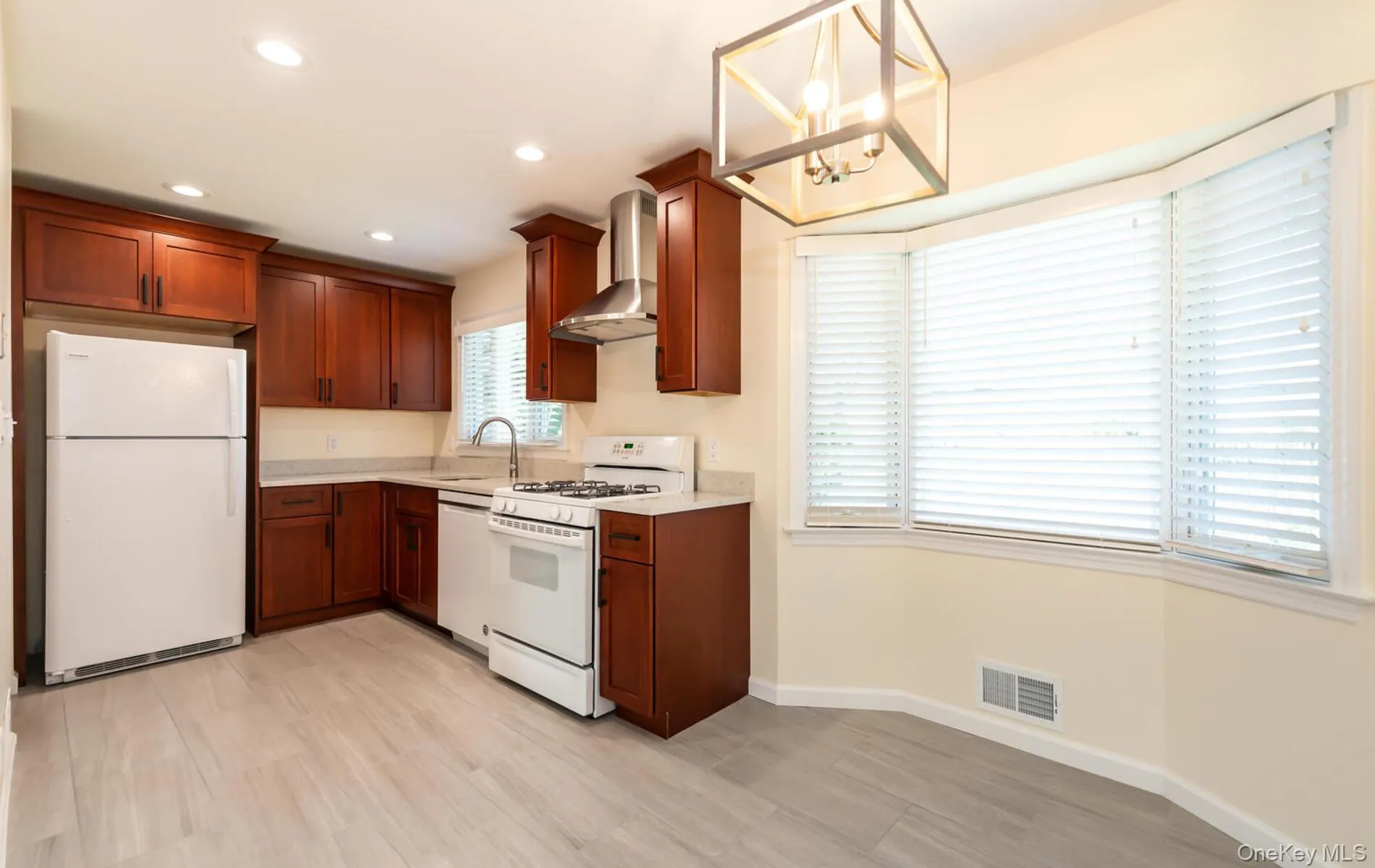 Kitchen featuring white appliances, a chandelier, wall chimney range hood, hanging light fixtures, and recessed lighting Kitchen featuring white appliances, a chandelier, wall chimney range hood, hanging light fixtures, and recessed lighting