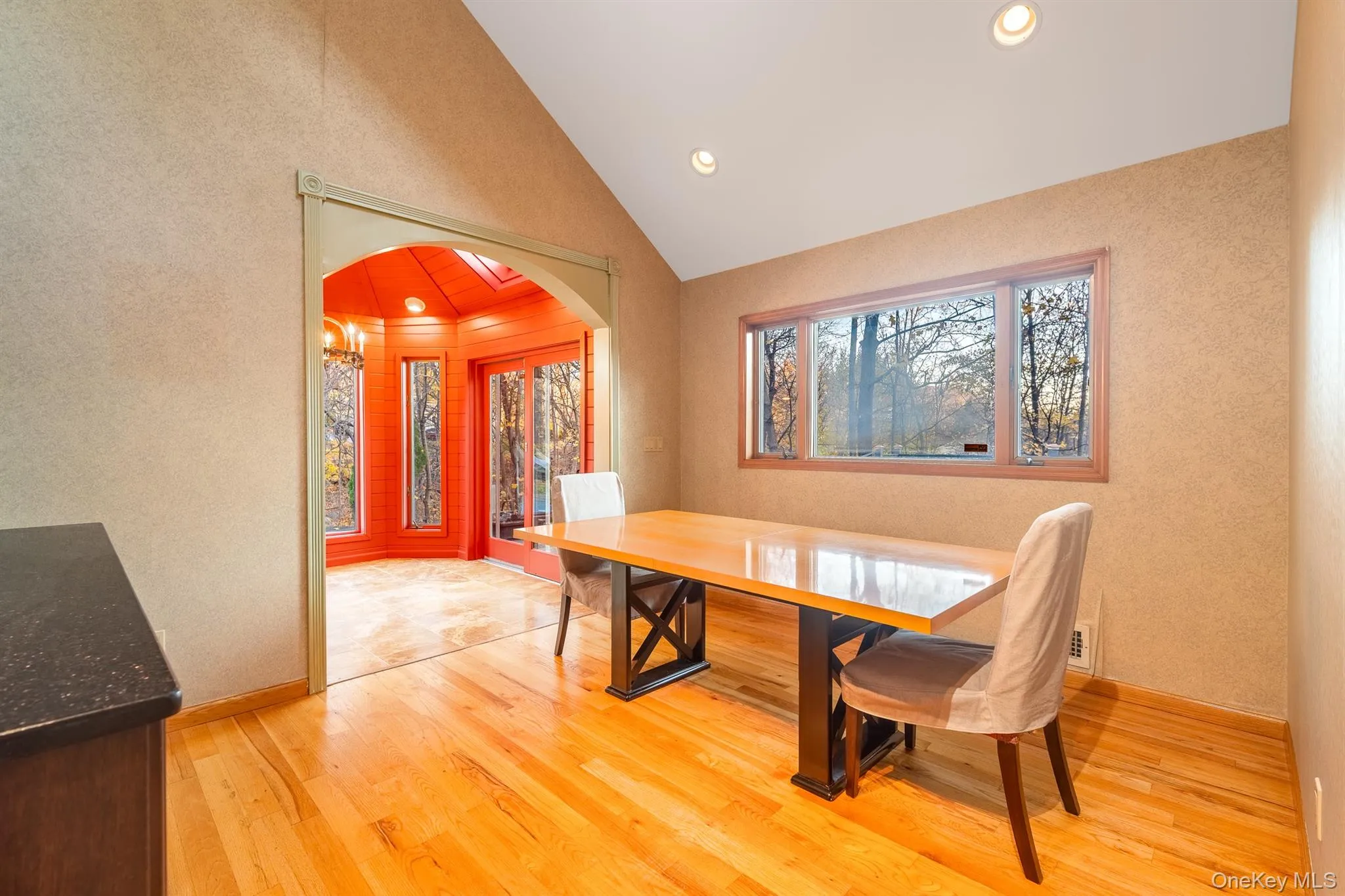 Dining space featuring arched walkways, light wood finished floors, a textured wall, healthy amount of natural light, and vaulted ceiling Dining space featuring arched walkways, light wood finished floors, a textured wall, healthy amount of natural light, and vaulted ceiling
