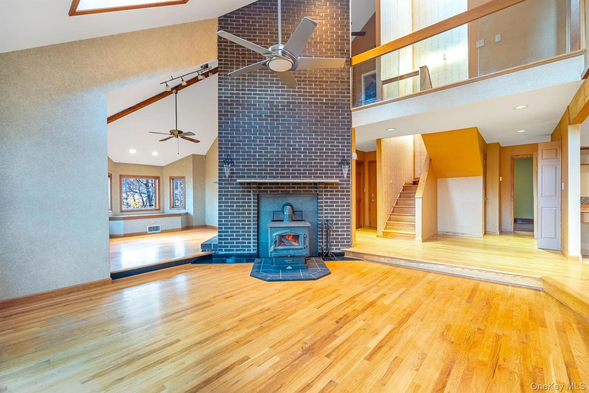 Unfurnished living room featuring wood finished floors, a wood stove, stairs, high vaulted ceiling, and recessed lighting Unfurnished living room featuring wood finished floors, a wood stove, stairs, high vaulted ceiling, and recessed lighting