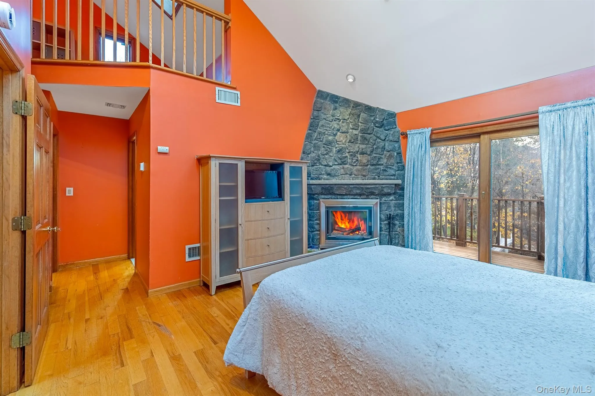 Bedroom with multiple windows, light wood-type flooring, access to exterior, a stone fireplace, and high vaulted ceiling Bedroom with multiple windows, light wood-type flooring, access to exterior, a stone fireplace, and high vaulted ceiling