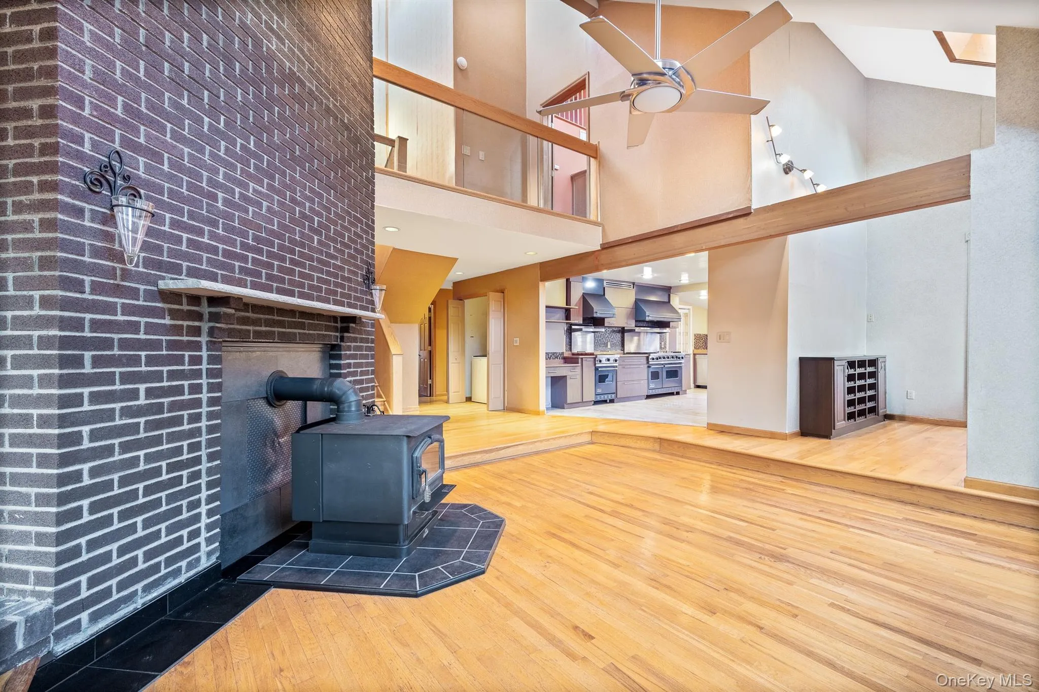 Unfurnished living room with a wood stove, brick wall, wood-type flooring, a high ceiling, and ceiling fan Unfurnished living room with a wood stove, brick wall, wood-type flooring, a high ceiling, and ceiling fan