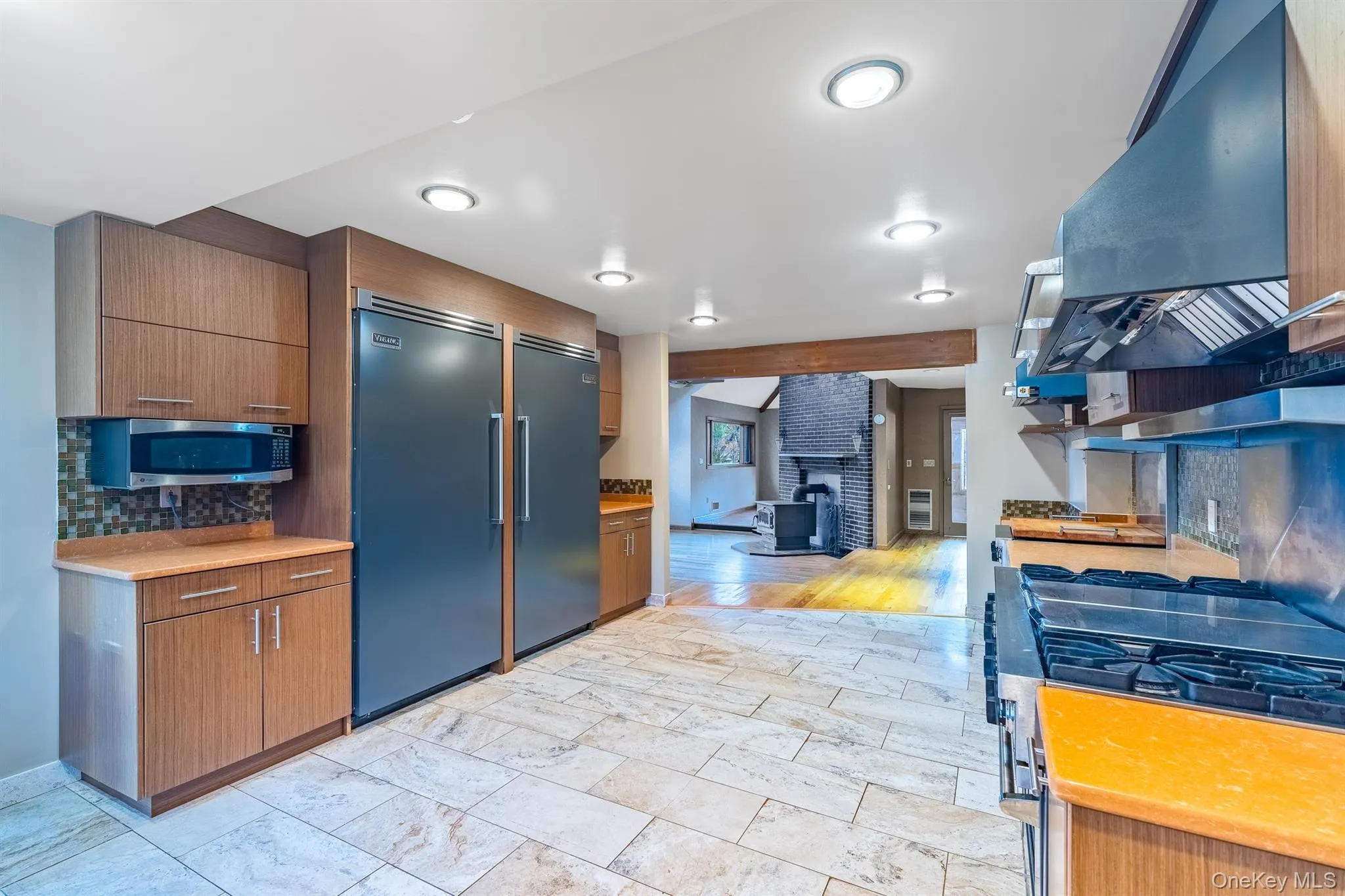 Kitchen featuring tasteful backsplash, appliances with stainless steel finishes, ventilation hood, brown cabinetry, and modern cabinets Kitchen featuring tasteful backsplash, appliances with stainless steel finishes, ventilation hood, brown cabinetry, and modern cabinets
