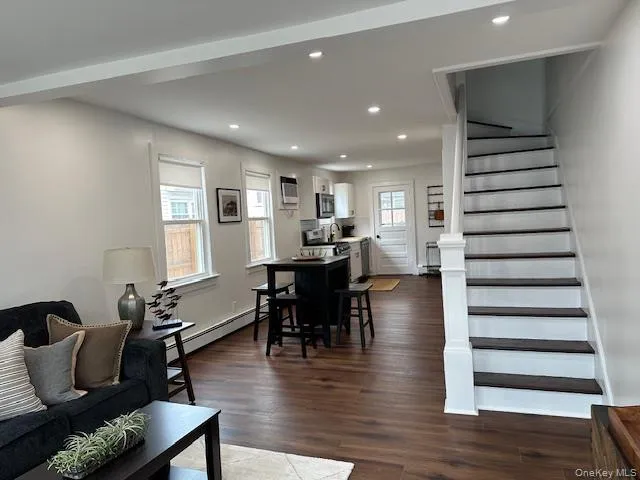 Living area with baseboard heating, recessed lighting, plenty of natural light, dark wood finished floors, and stairway Living area with baseboard heating, recessed lighting, plenty of natural light, dark wood finished floors, and stairway