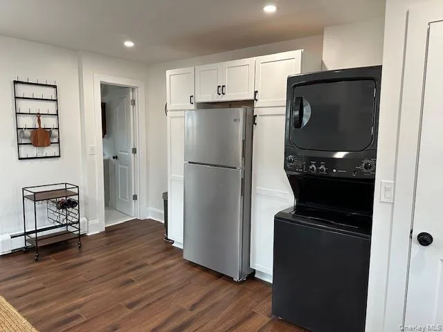 Kitchen featuring white cabinets, freestanding refrigerator, baseboard heating, dark wood-style floors, and stacked washer / dryer Kitchen featuring white cabinets, freestanding refrigerator, baseboard heating, dark wood-style floors, and stacked washer / dryer
