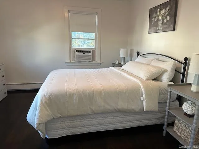 Bedroom featuring dark wood-style floors, a baseboard heating unit, and cooling unit Bedroom featuring dark wood-style floors, a baseboard heating unit, and cooling unit