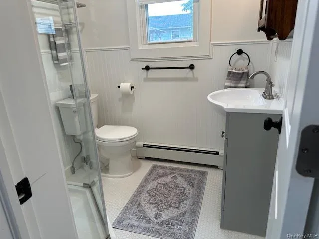 Bathroom with vanity, wainscoting, a baseboard heating unit, and a stall shower Bathroom with vanity, wainscoting, a baseboard heating unit, and a stall shower