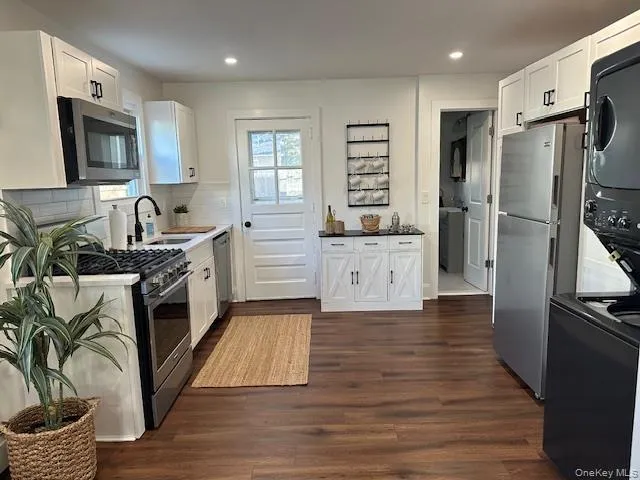 Kitchen featuring white cabinetry, stainless steel appliances, dark wood-style floors, stacked washer / drying machine, and recessed lighting Kitchen featuring white cabinetry, stainless steel appliances, dark wood-style floors, stacked washer / drying machine, and recessed lighting
