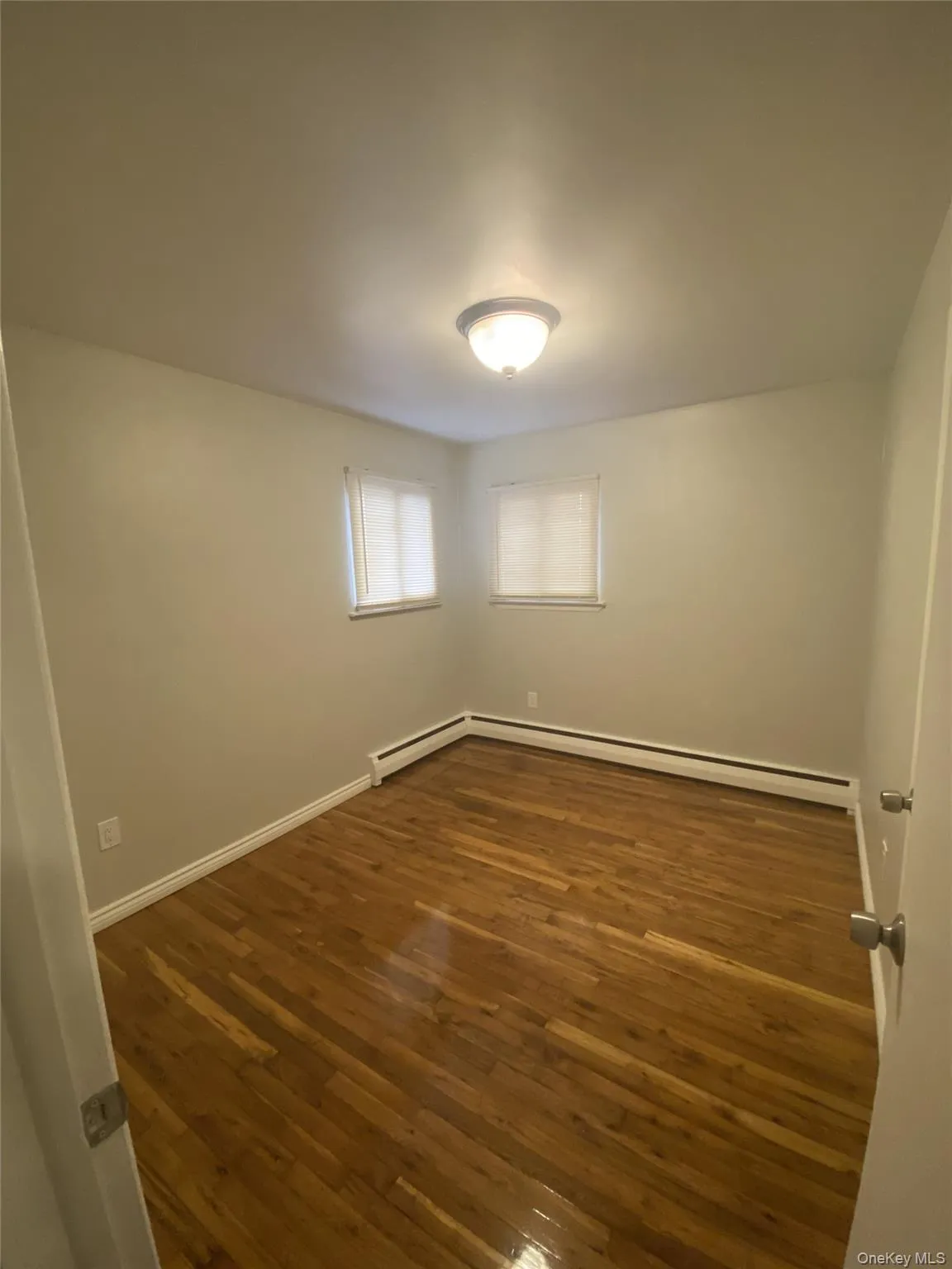 Empty room featuring dark wood-type flooring and a baseboard radiator Empty room featuring dark wood-type flooring and a baseboard radiator