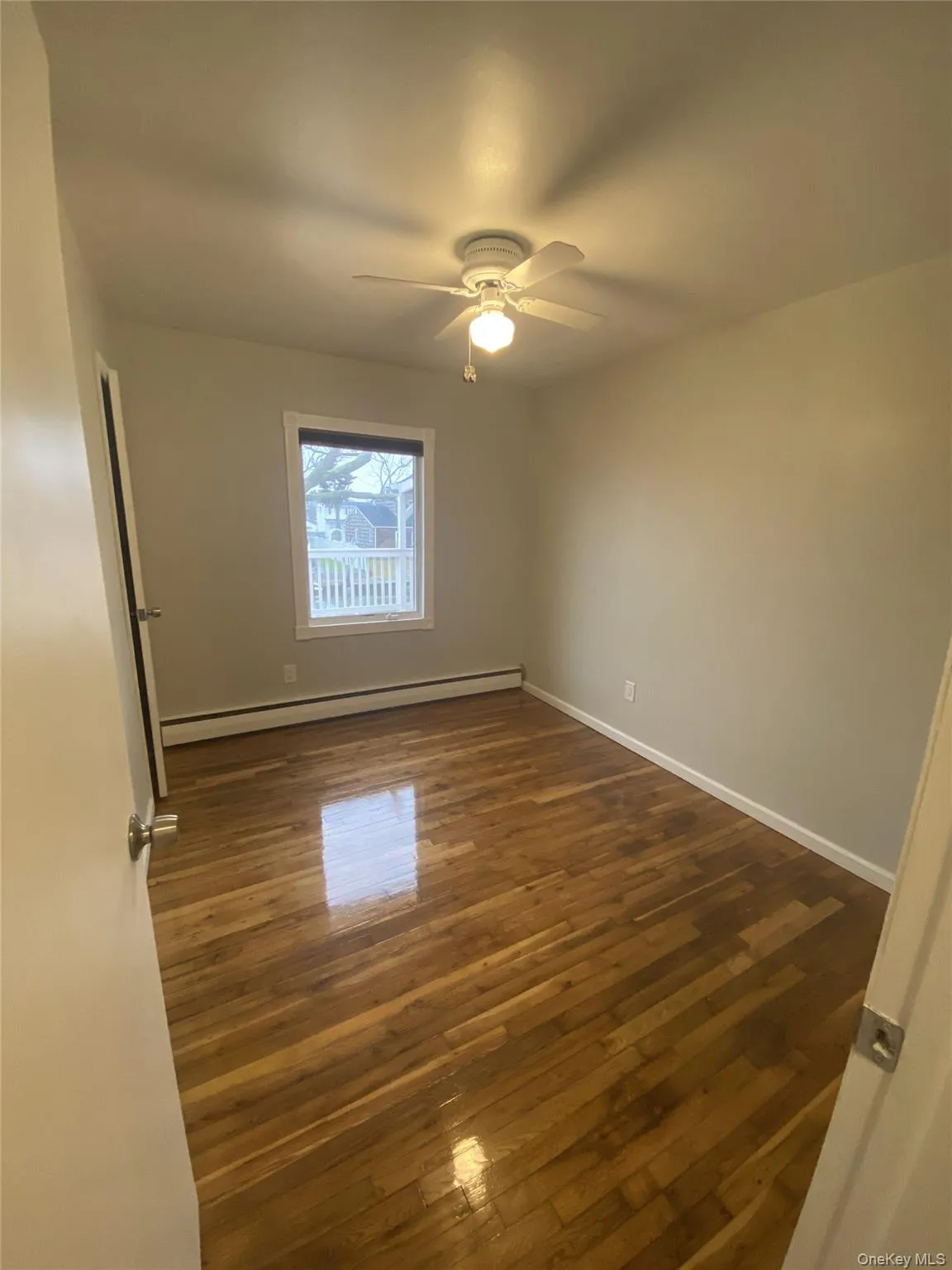 Unfurnished room with a baseboard heating unit, dark wood-type flooring, and a ceiling fan Unfurnished room with a baseboard heating unit, dark wood-type flooring, and a ceiling fan