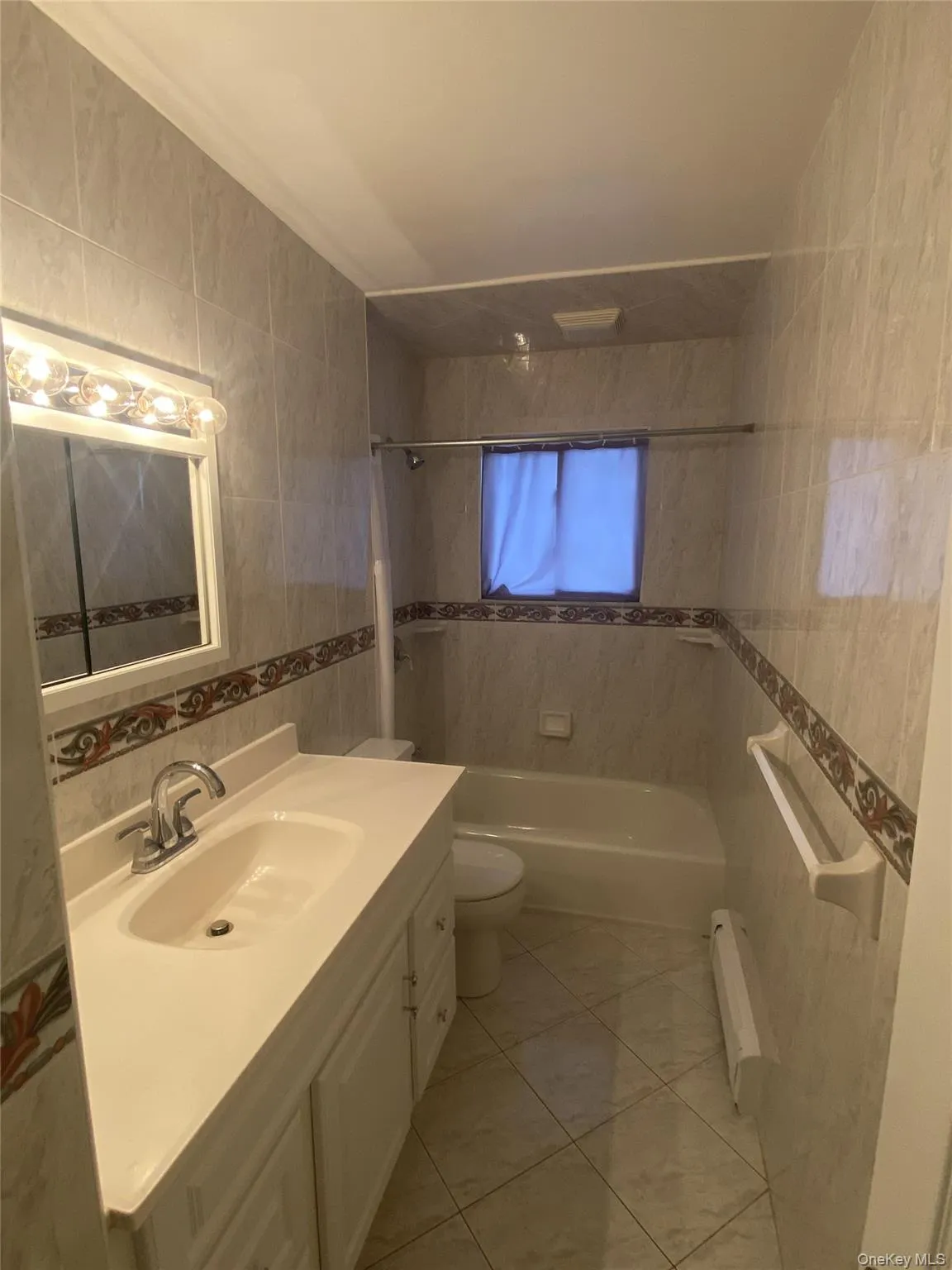 Full bath featuring tile walls, bathing tub / shower combination, vanity, baseboard heating, and light tile patterned flooring Full bath featuring tile walls, bathing tub / shower combination, vanity, baseboard heating, and light tile patterned flooring