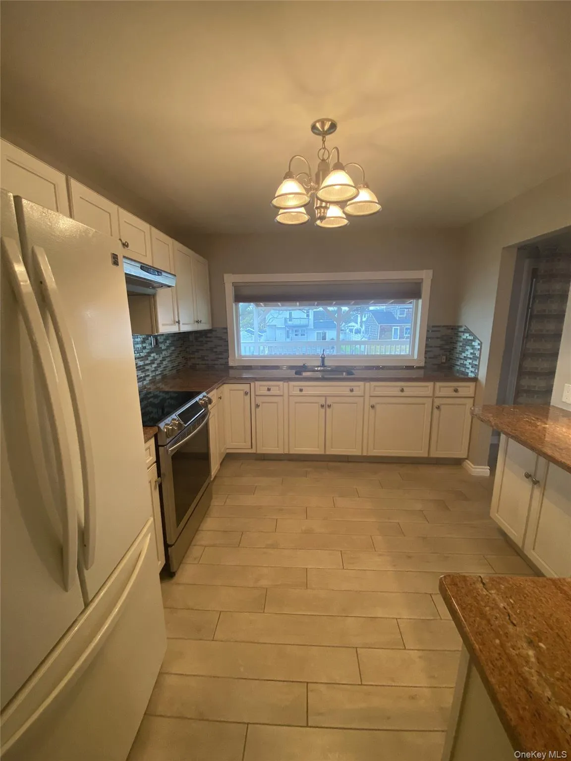 Kitchen with freestanding refrigerator, white cabinetry, stainless steel electric range, pendant lighting, and decorative backsplash Kitchen with freestanding refrigerator, white cabinetry, stainless steel electric range, pendant lighting, and decorative backsplash