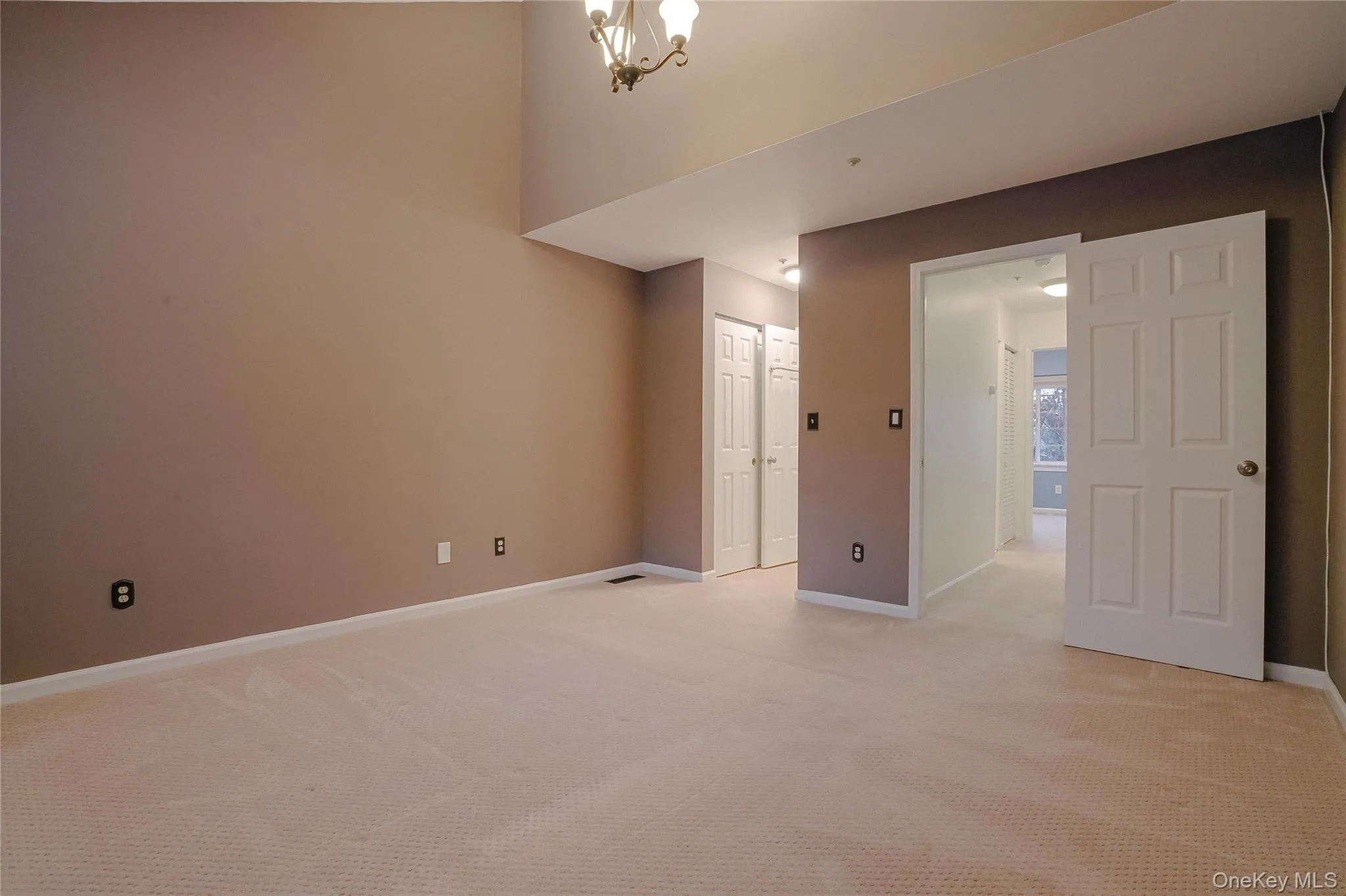Empty room featuring light colored carpet and a chandelier Empty room featuring light colored carpet and a chandelier