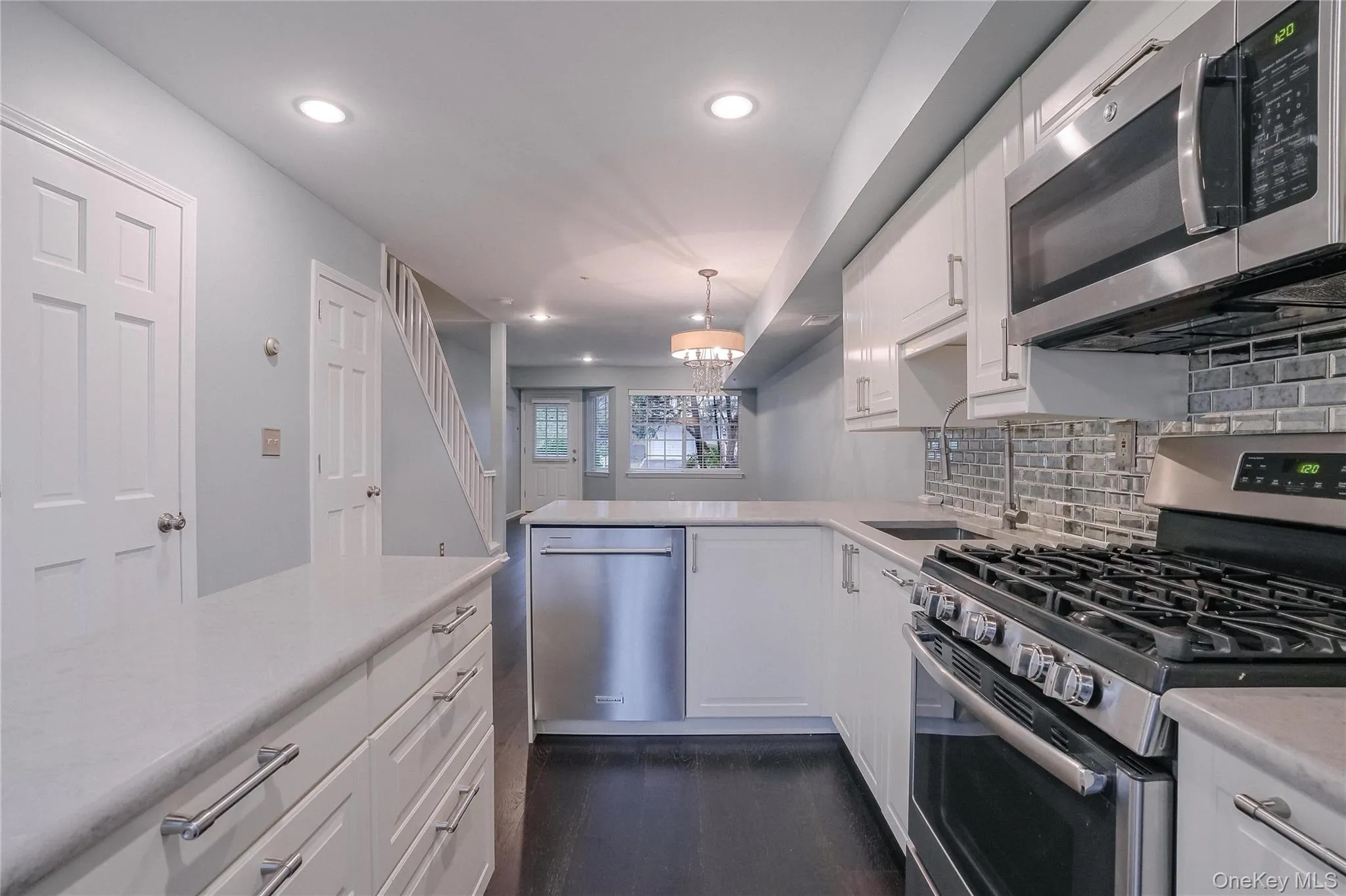 Kitchen featuring white cabinets, appliances with stainless steel finishes, hanging light fixtures, backsplash, and a chandelier Kitchen featuring white cabinets, appliances with stainless steel finishes, hanging light fixtures, backsplash, and a chandelier