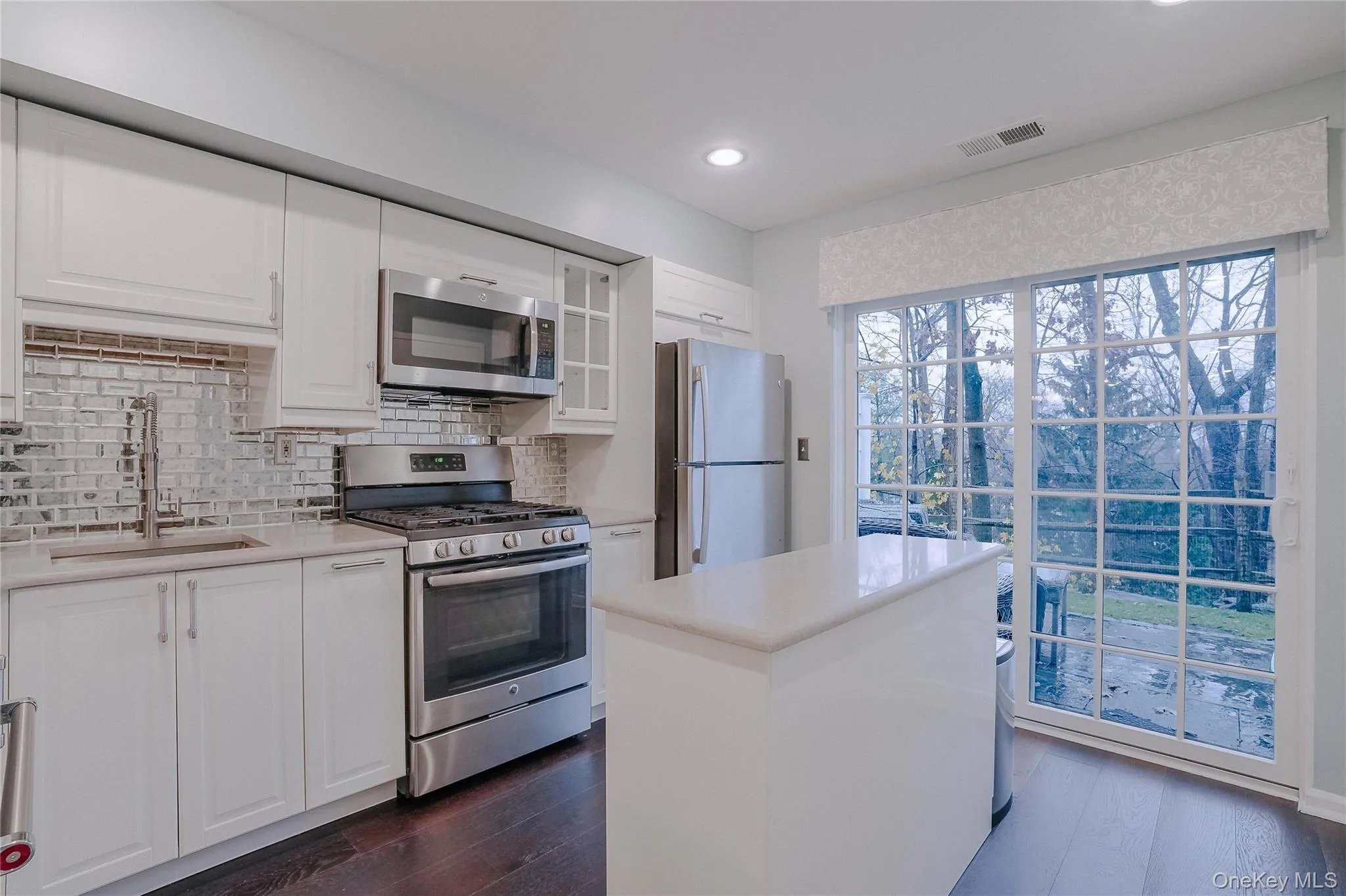 Kitchen featuring appliances with stainless steel finishes, white cabinetry, a kitchen island, tasteful backsplash, and glass insert cabinets Kitchen featuring appliances with stainless steel finishes, white cabinetry, a kitchen island, tasteful backsplash, and glass insert cabinets