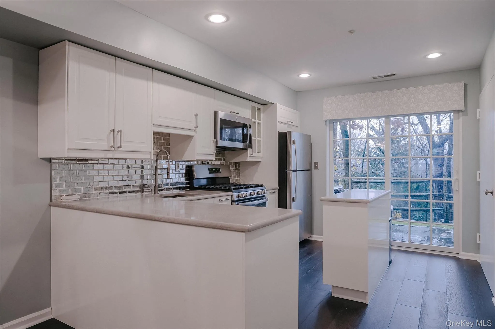 Kitchen featuring appliances with stainless steel finishes, white cabinets, tasteful backsplash, a peninsula, and dark wood-style floors Kitchen featuring appliances with stainless steel finishes, white cabinets, tasteful backsplash, a peninsula, and dark wood-style floors
