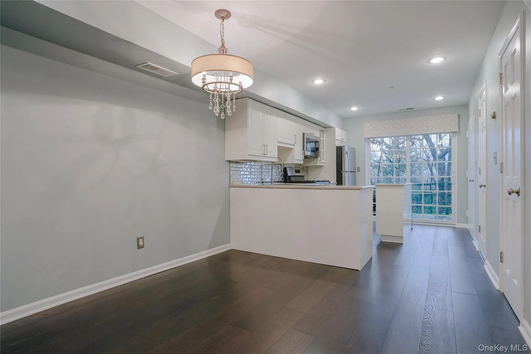 Kitchen with white cabinets, backsplash, hanging light fixtures, a peninsula, and a chandelier Kitchen with white cabinets, backsplash, hanging light fixtures, a peninsula, and a chandelier