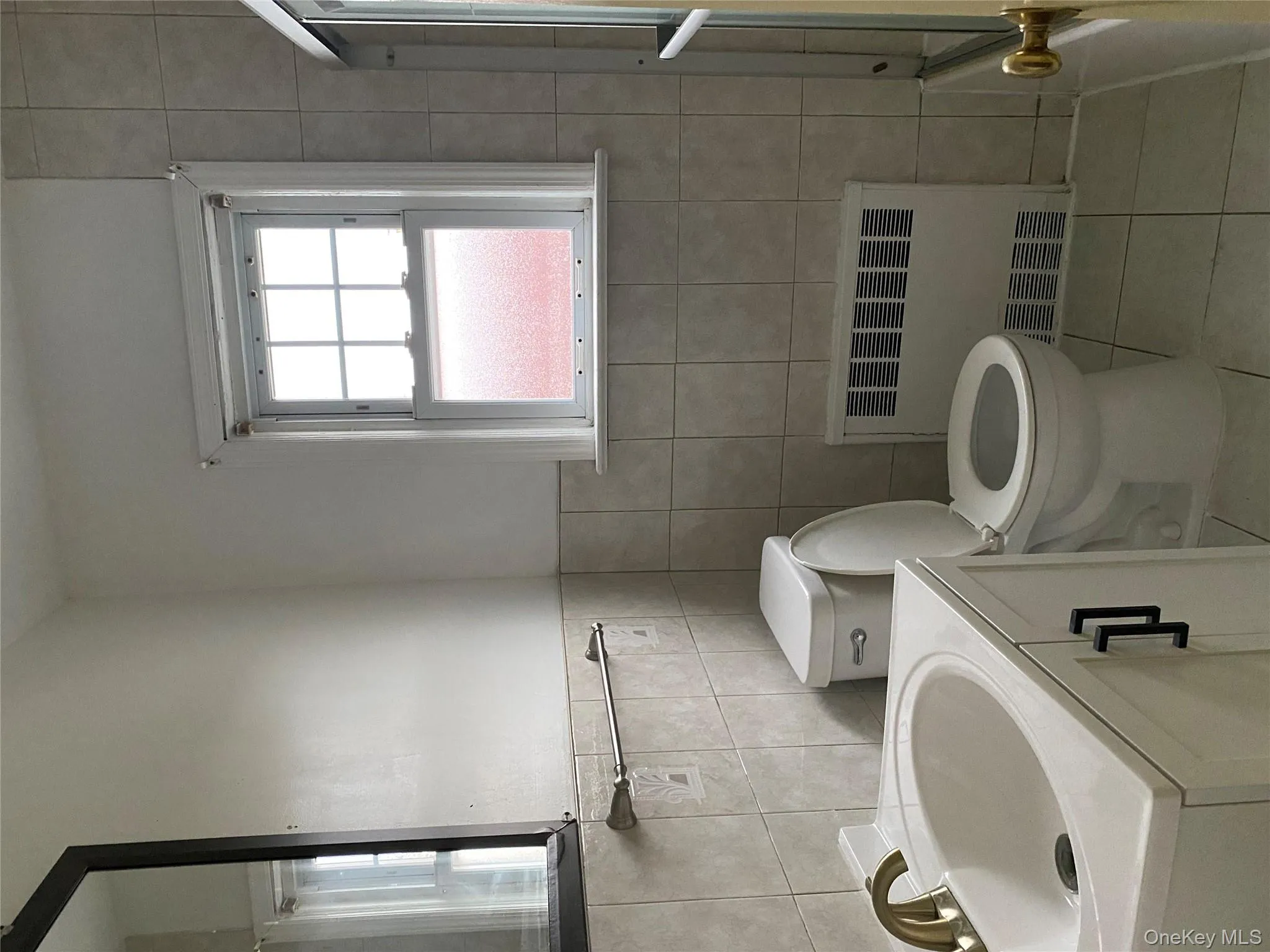 Full bathroom with radiator heating unit, vanity, light tile patterned flooring, shower / bath combination with glass door, and tile walls Full bathroom with radiator heating unit, vanity, light tile patterned flooring, shower / bath combination with glass door, and tile walls