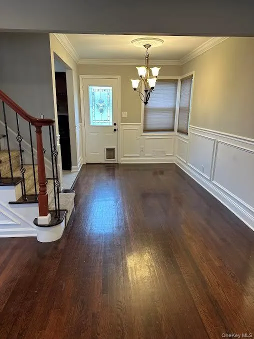 Unfurnished dining area with a decorative wall, stairs, a wainscoted wall, dark wood-style flooring, and crown molding Unfurnished dining area with a decorative wall, stairs, a wainscoted wall, dark wood-style flooring, and crown molding