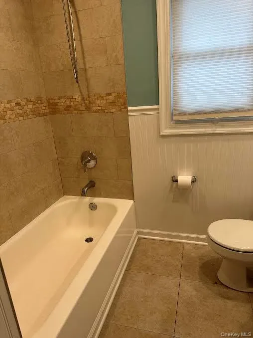 Bathroom featuring a wainscoted wall, shower combination, and light tile patterned floors Bathroom featuring a wainscoted wall, shower combination, and light tile patterned floors