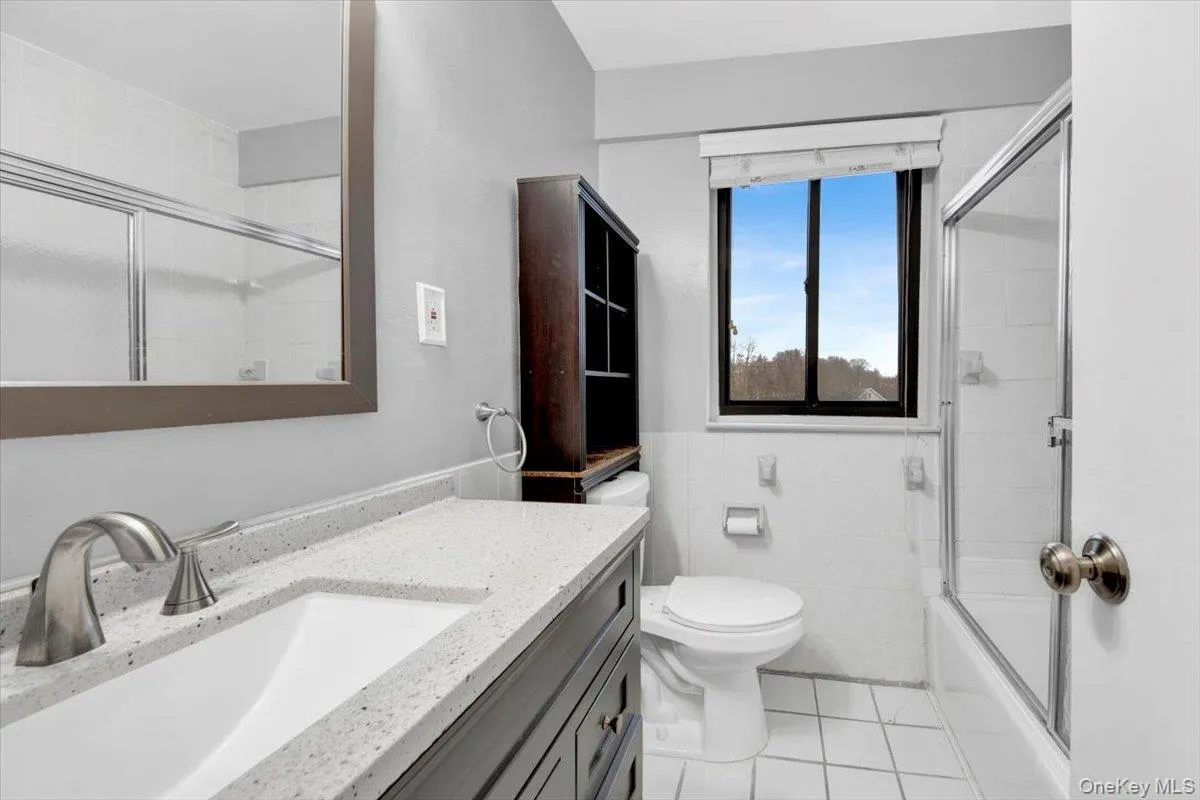 Full bathroom featuring vanity, light tile patterned floors, tile walls, and enclosed tub / shower combo Full bathroom featuring vanity, light tile patterned floors, tile walls, and enclosed tub / shower combo