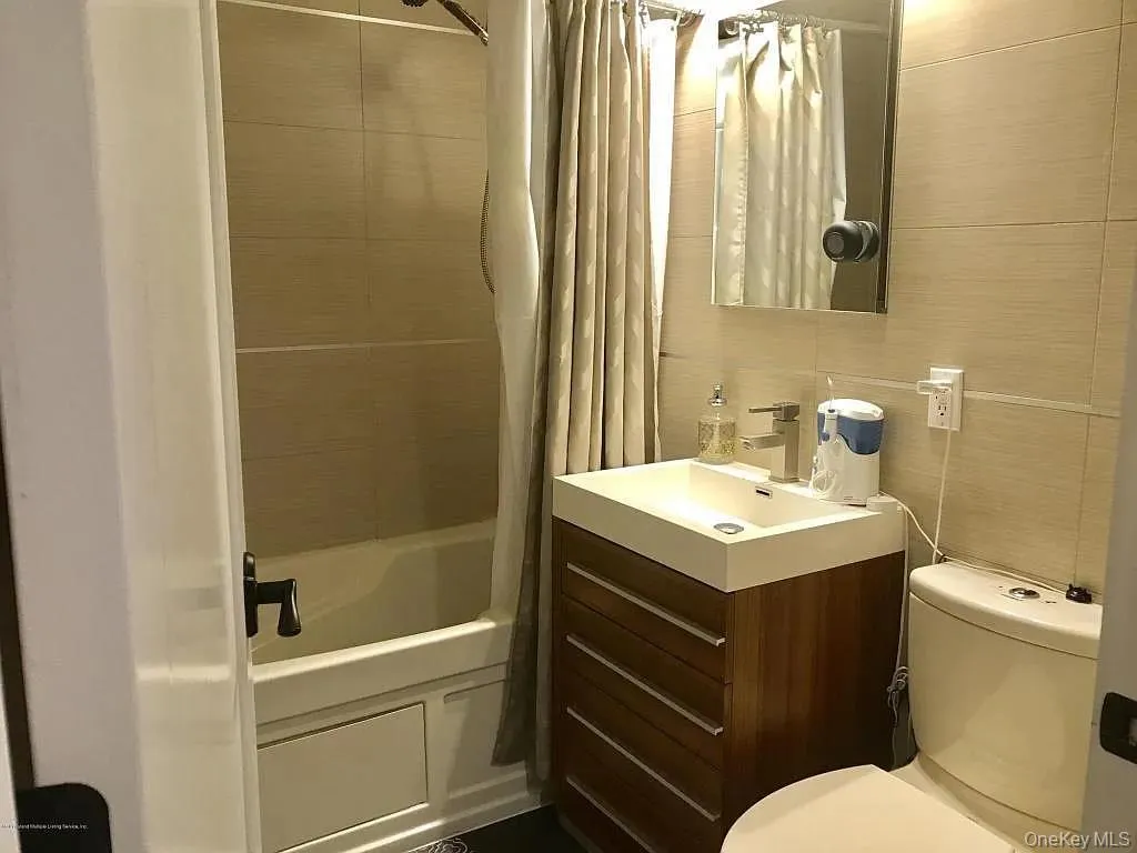 Bathroom featuring vanity, shower / tub combo with curtain, and tile walls Bathroom featuring vanity, shower / tub combo with curtain, and tile walls