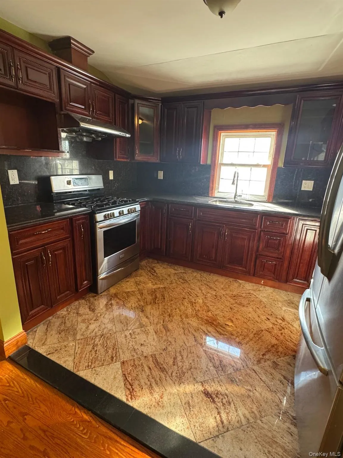 Kitchen with glass insert cabinets, appliances with stainless steel finishes, under cabinet range hood, decorative backsplash, and reddish brown cabinets Kitchen with glass insert cabinets, appliances with stainless steel finishes, under cabinet range hood, decorative backsplash, and reddish brown cabinets