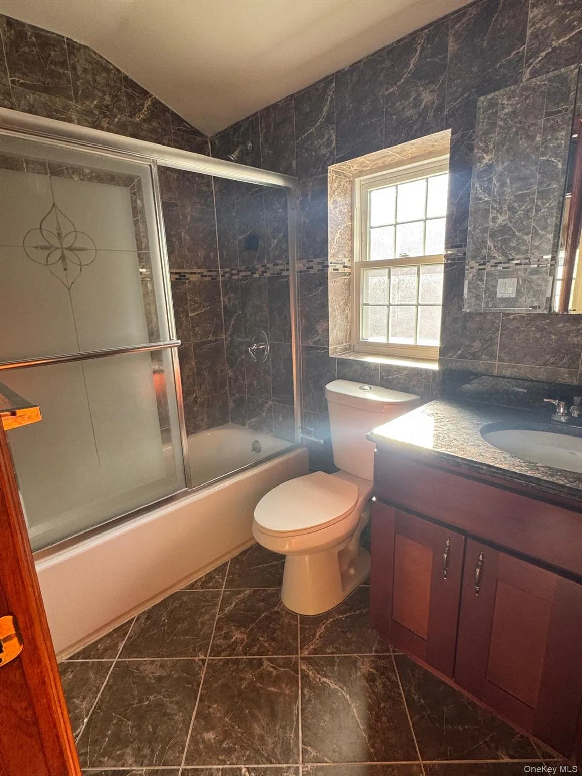 Full bathroom featuring vanity, tile walls, enclosed tub / shower combo, dark marble finish floors, and lofted ceiling Full bathroom featuring vanity, tile walls, enclosed tub / shower combo, dark marble finish floors, and lofted ceiling