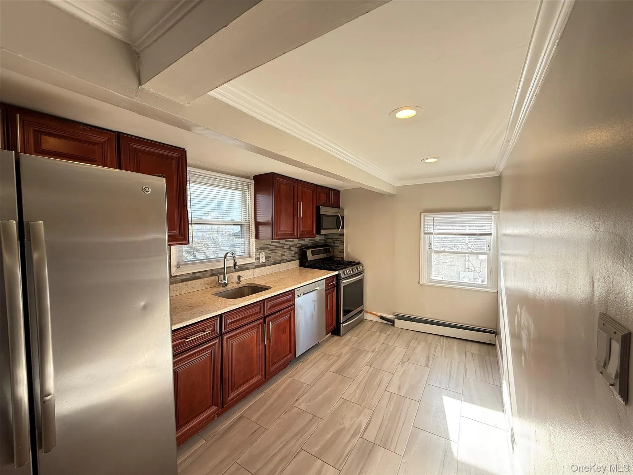 Kitchen with stainless steel appliances, ornamental molding, light stone counters, baseboard heating, and decorative backsplash Kitchen with stainless steel appliances, ornamental molding, light stone counters, baseboard heating, and decorative backsplash