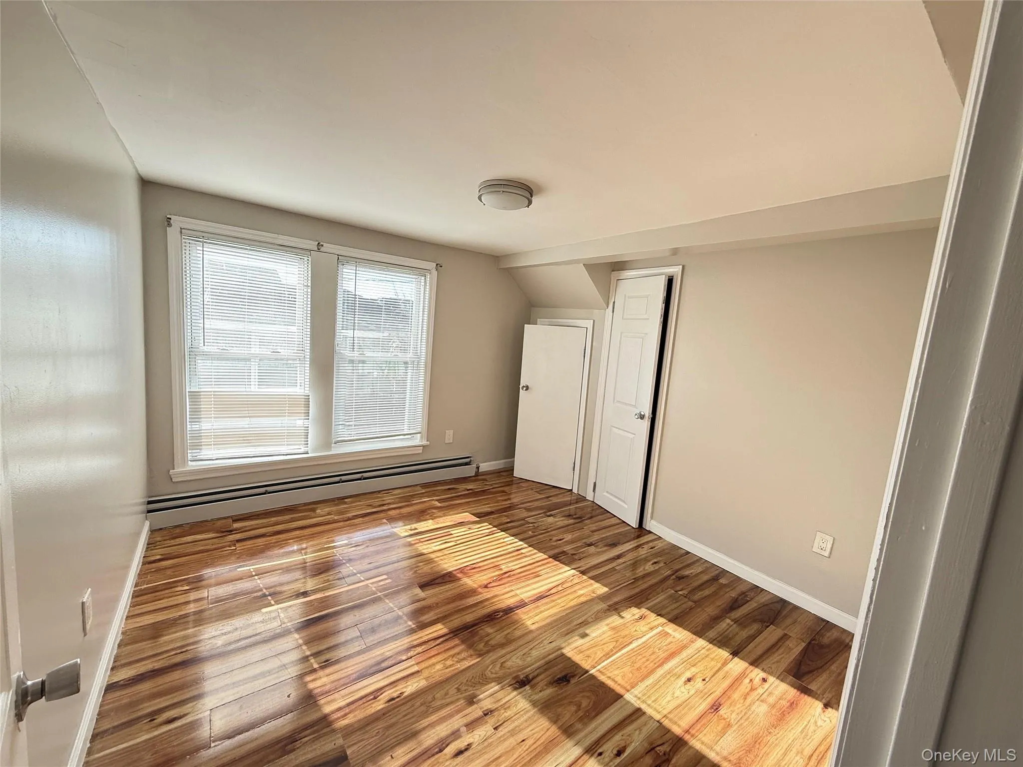 Unfurnished bedroom featuring a baseboard heating unit, light wood-style flooring, and lofted ceiling Unfurnished bedroom featuring a baseboard heating unit, light wood-style flooring, and lofted ceiling