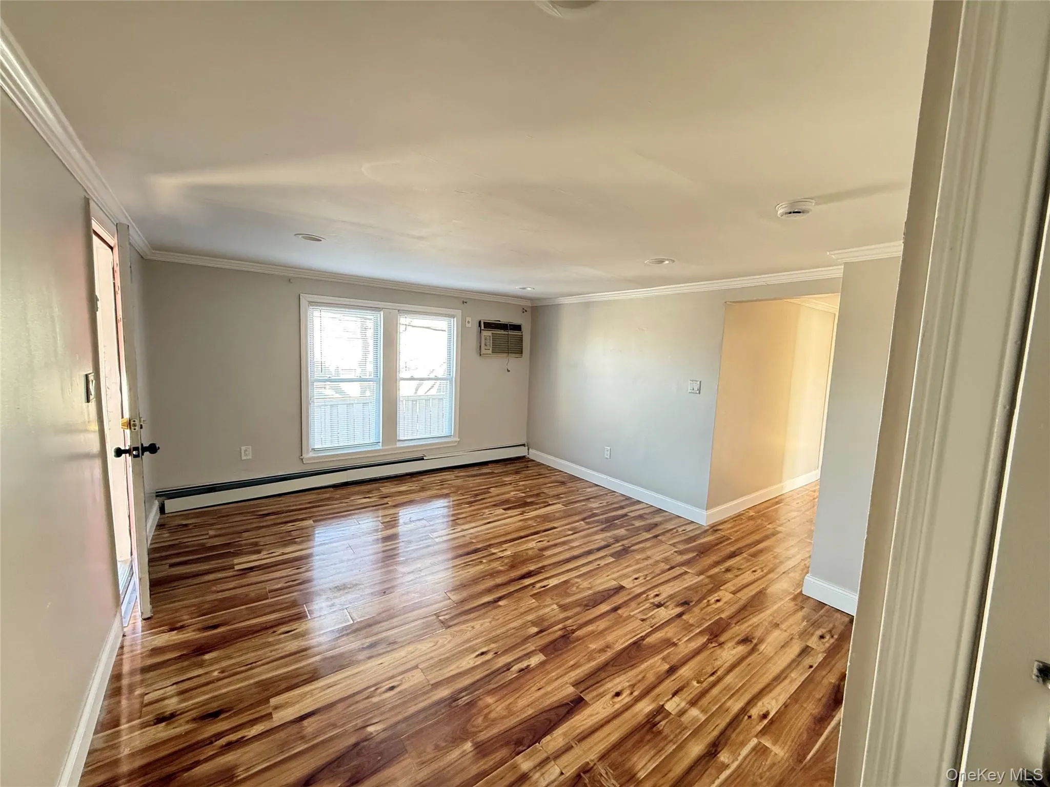 Unfurnished room featuring light wood-style flooring, ornamental molding, baseboard heating, and a wall mounted air conditioner Unfurnished room featuring light wood-style flooring, ornamental molding, baseboard heating, and a wall mounted air conditioner